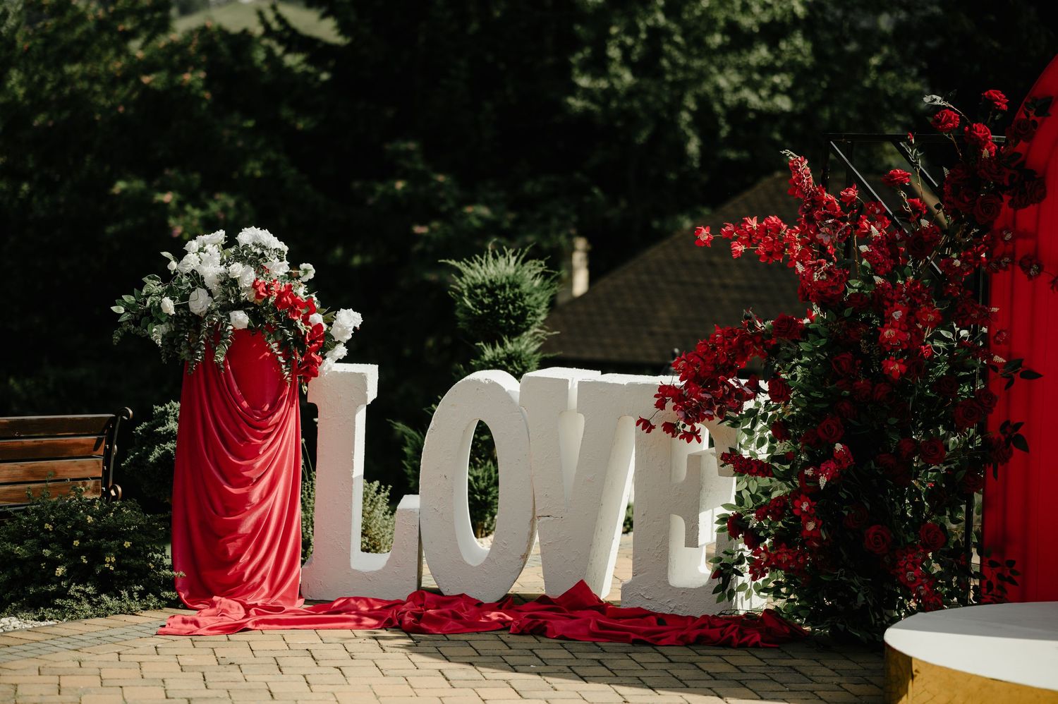 Large white LOVE letters with red and white floral arrangements displayed outdoors at a wedding venue.