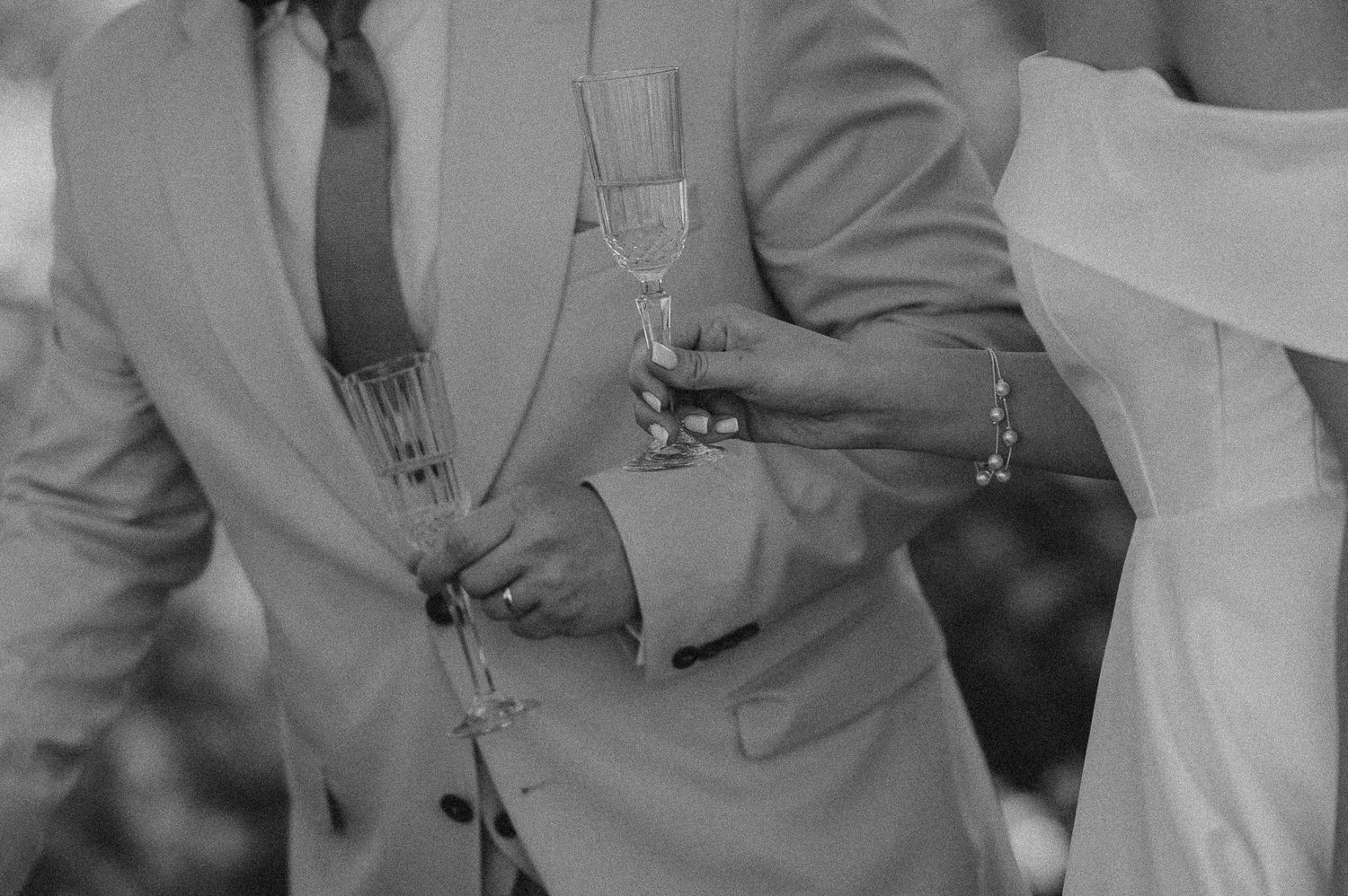 Black and white photo of wedding guests clinking champagne flutes at an outdoor reception.