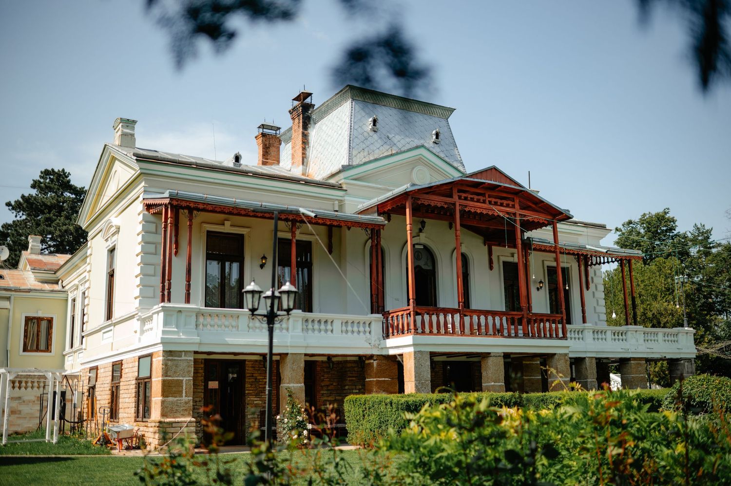 Historic Romanian villa wedding venue with white facade, red balcony railings, and lush garden surroundings.