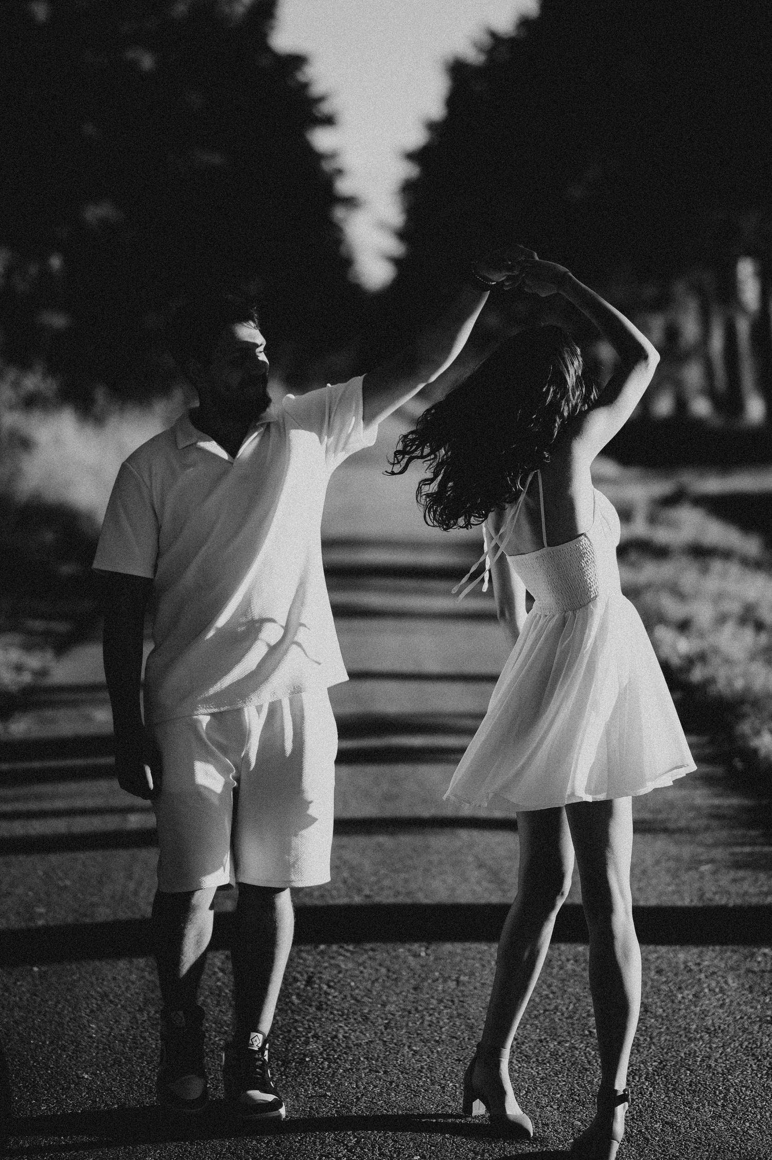 Black and white photo of couple dancing on a tree-lined road.