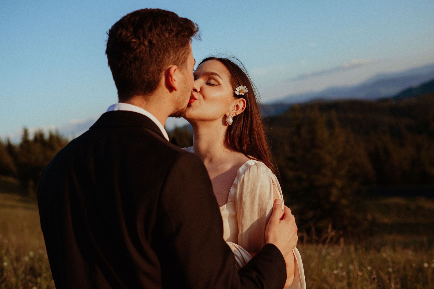 Bride and groom share a gentle kiss in a scenic mountain landscape at blue hour.