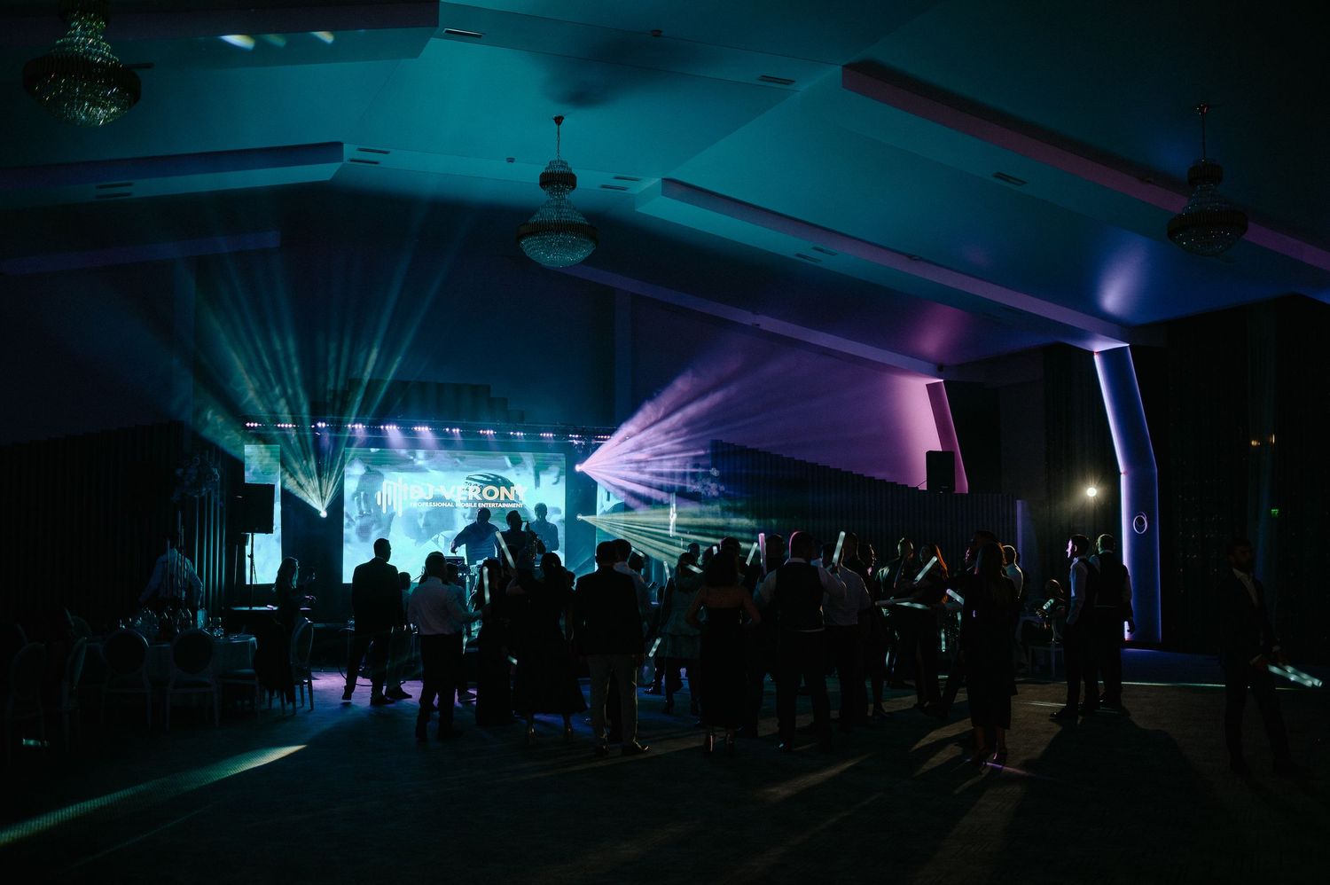 Dramatic wide-angle view of a wedding reception venue with laser lights and guests on the dance floor.