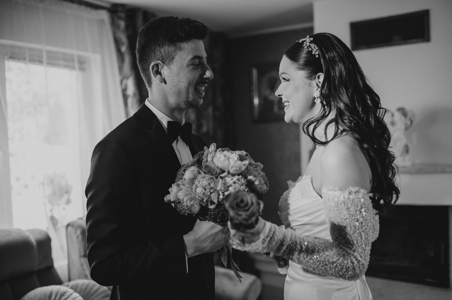Black and white photo of smiling bride and groom sharing a joyful moment holding a floral bouquet.