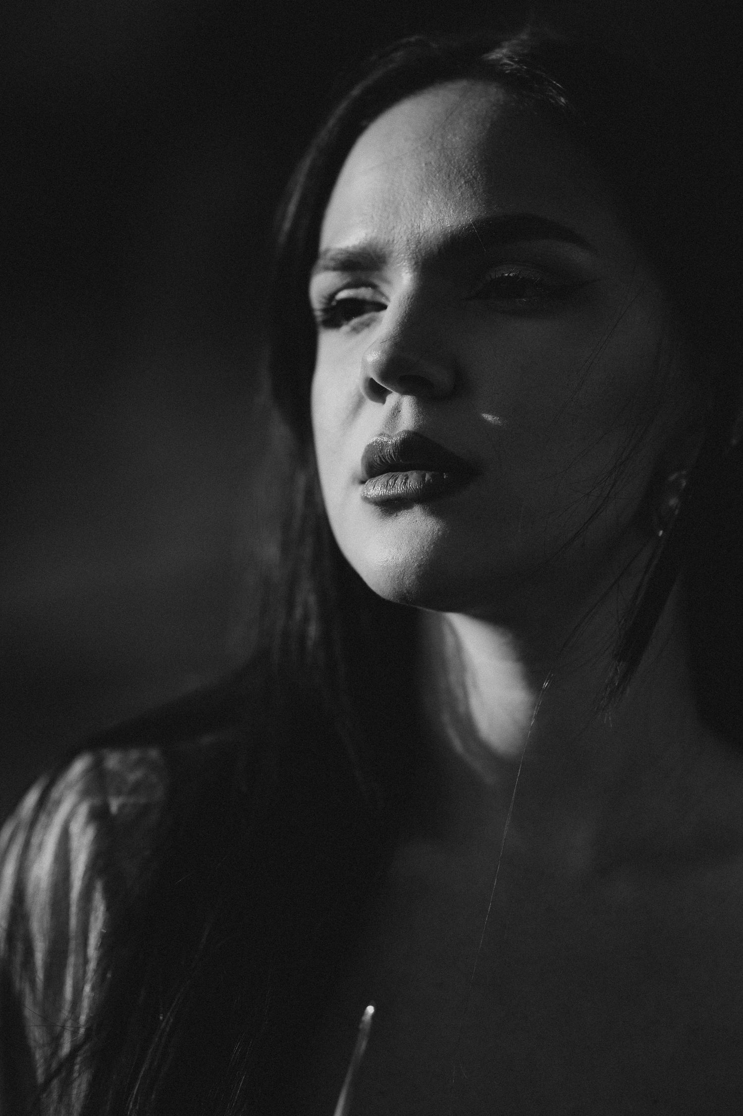 Dramatic black and white portrait of a young woman with long dark hair in moody lighting.