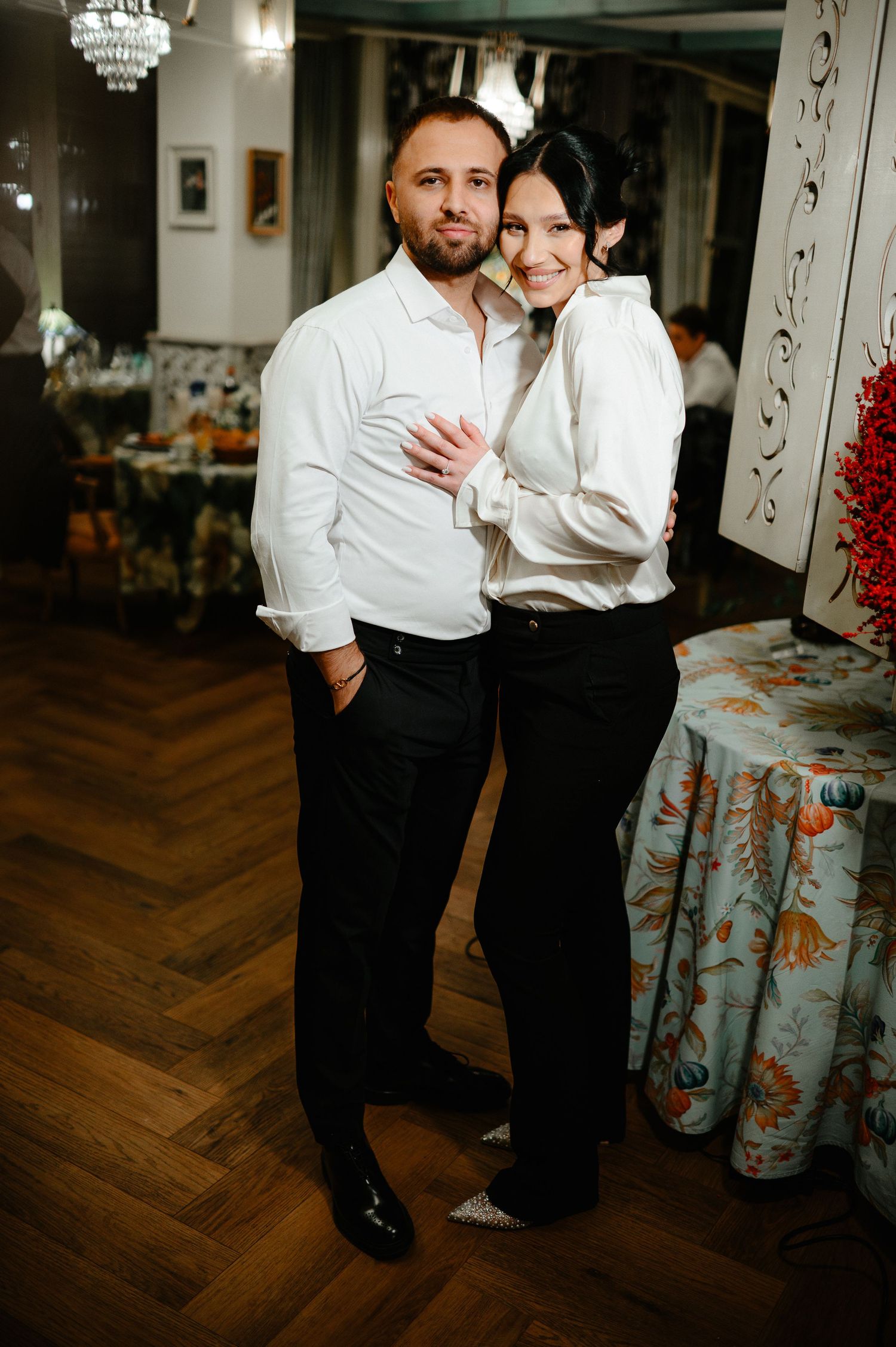 Happy wedding couple in matching white shirts and black pants pose together in elegant restaurant.