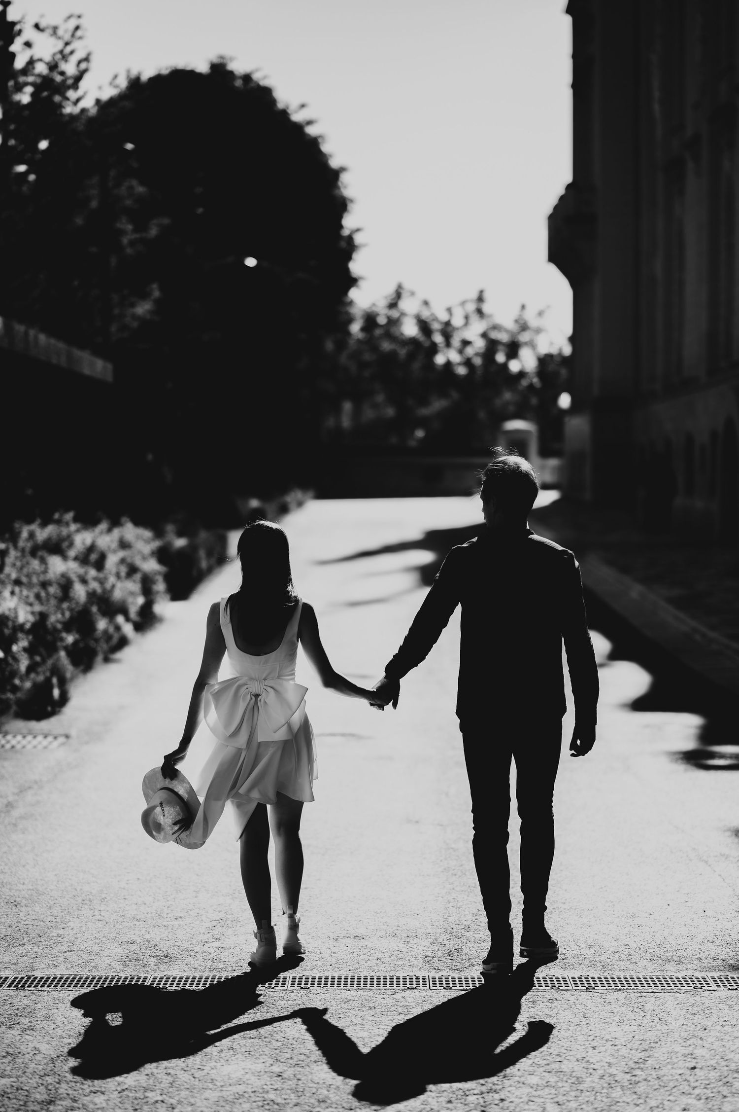 Black and white silhouette of a couple holding hands while walking down a sunny street.