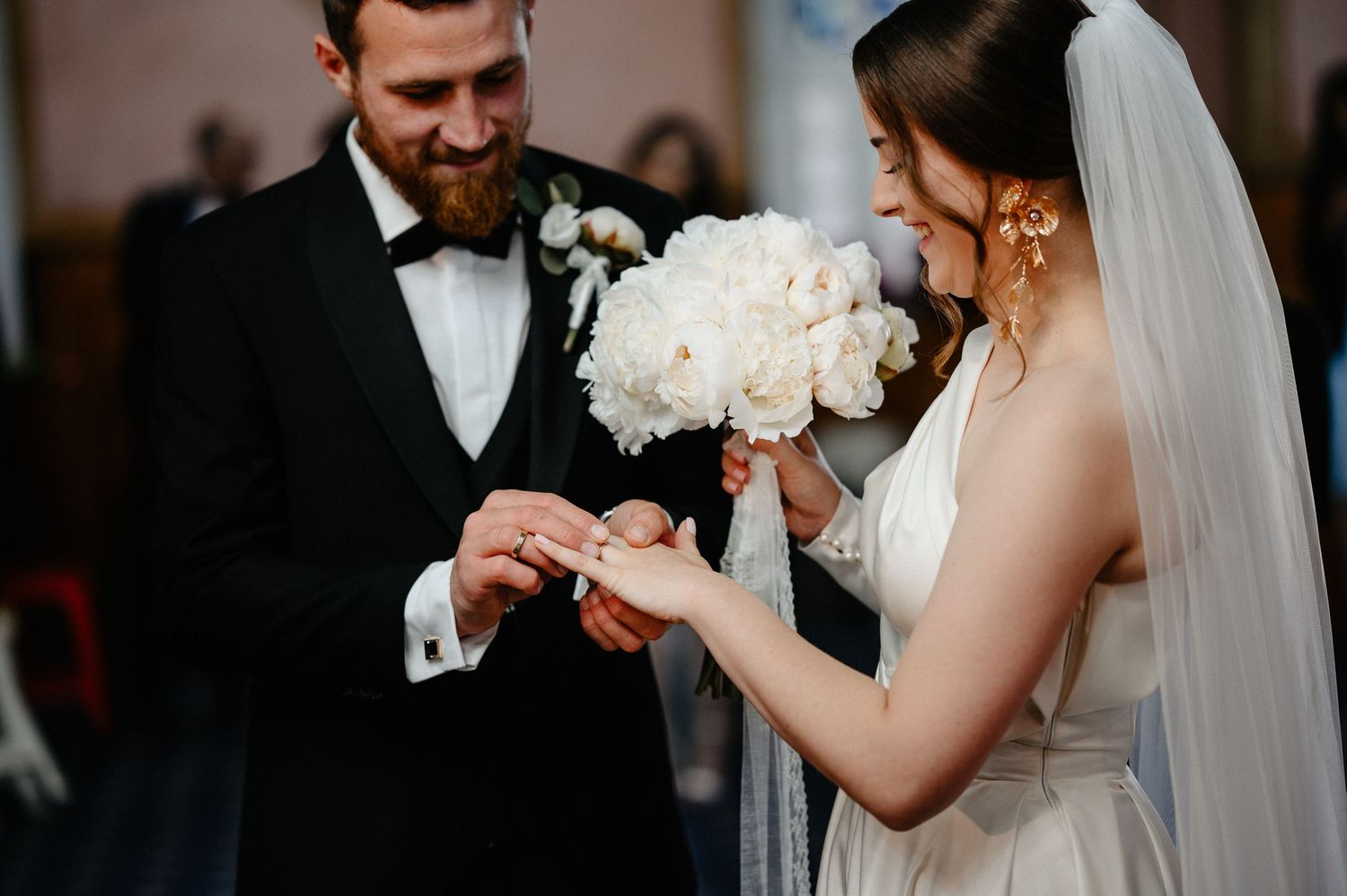Groom places wedding ring on bride's finger during intimate church ceremony exchange of vows.