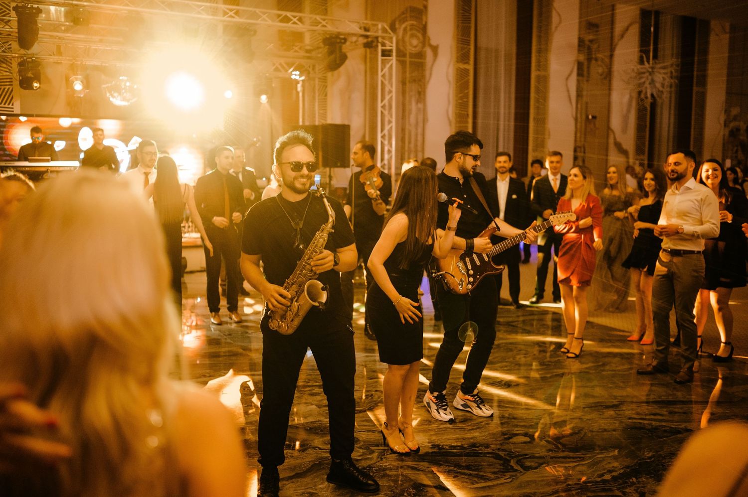 Saxophonist and guitarist performing live at an elegant wedding reception with guests dancing in a grand venue.