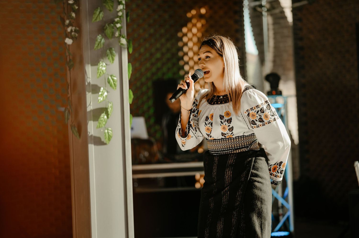 Young woman in embroidered Ukrainian blouse singing passionately into a microphone on stage.