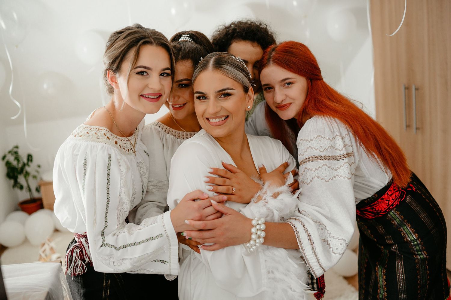 Bride in white robe smiling with four bridesmaids in traditional attire.