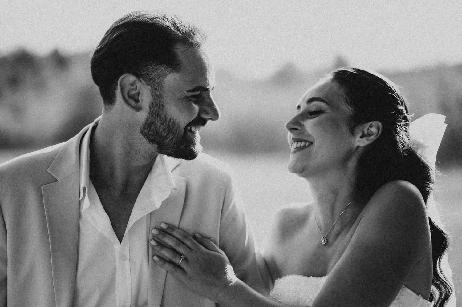 Black and white photo of laughing bride and groom sharing a joyful moment at outdoor wedding.