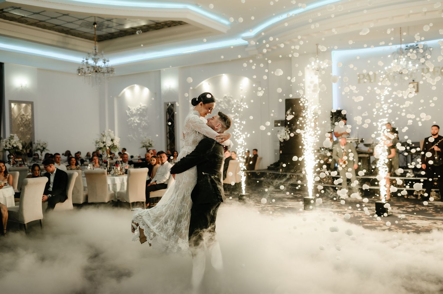 Couple sharing first dance on cloud-filled dance floor with confetti at elegant wedding reception.
