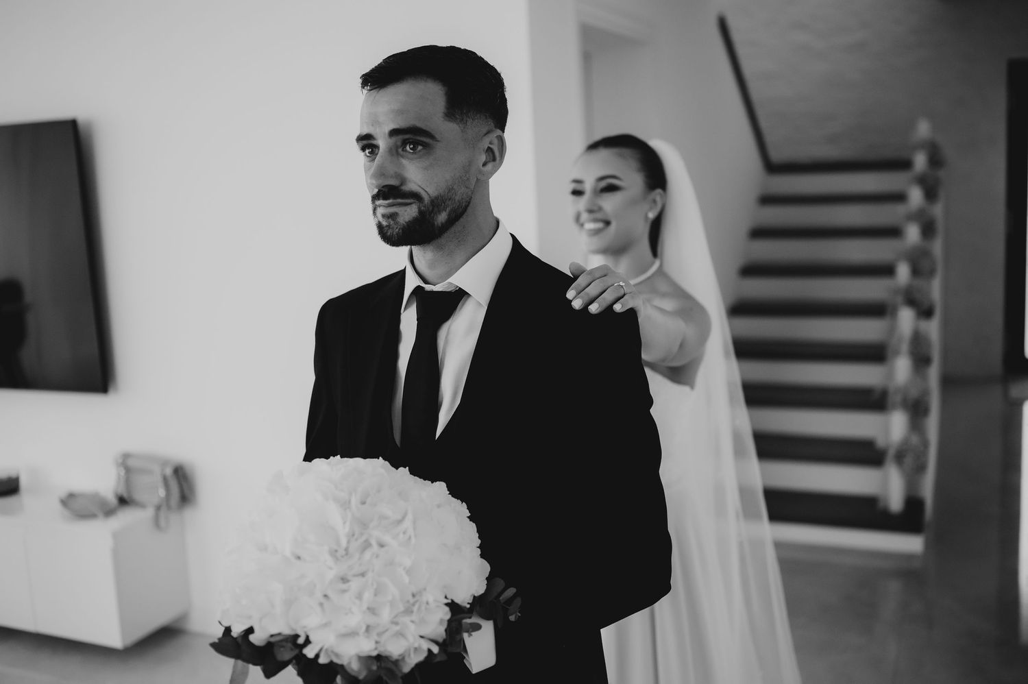 Black and white photo of bride placing hand on groom's shoulder during wedding first look moment.