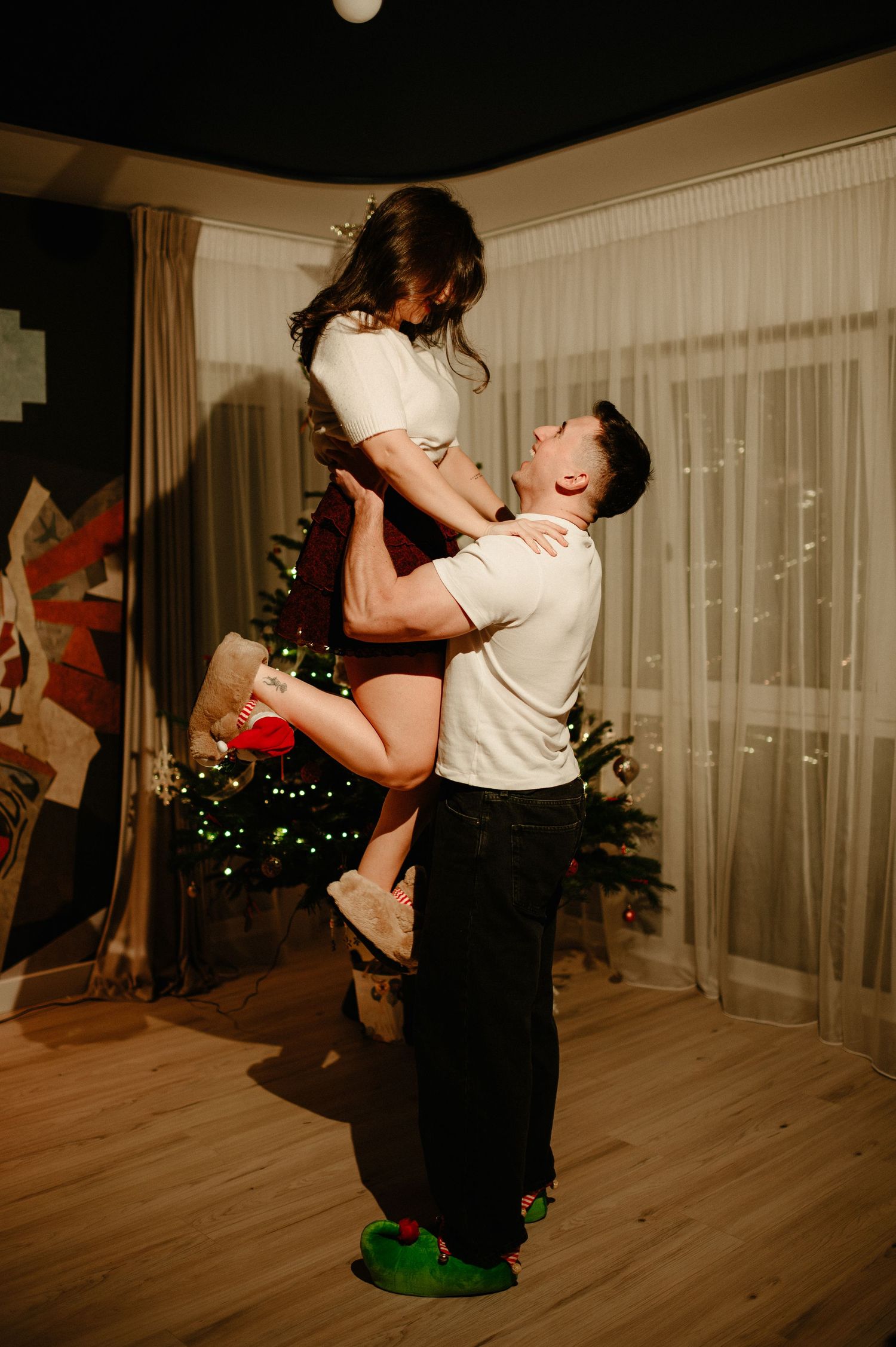 Man lifting woman joyfully in a festively decorated Christmas living room.