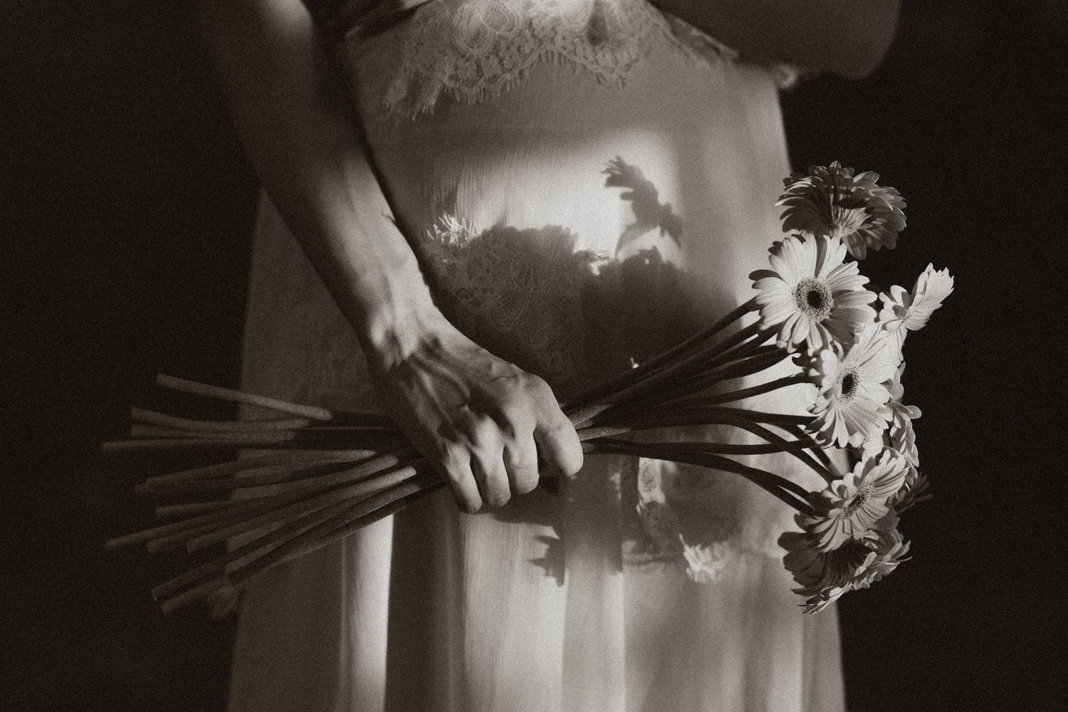 Black and white photo of a bride in white dress holding a bouquet of daisies with long stems.