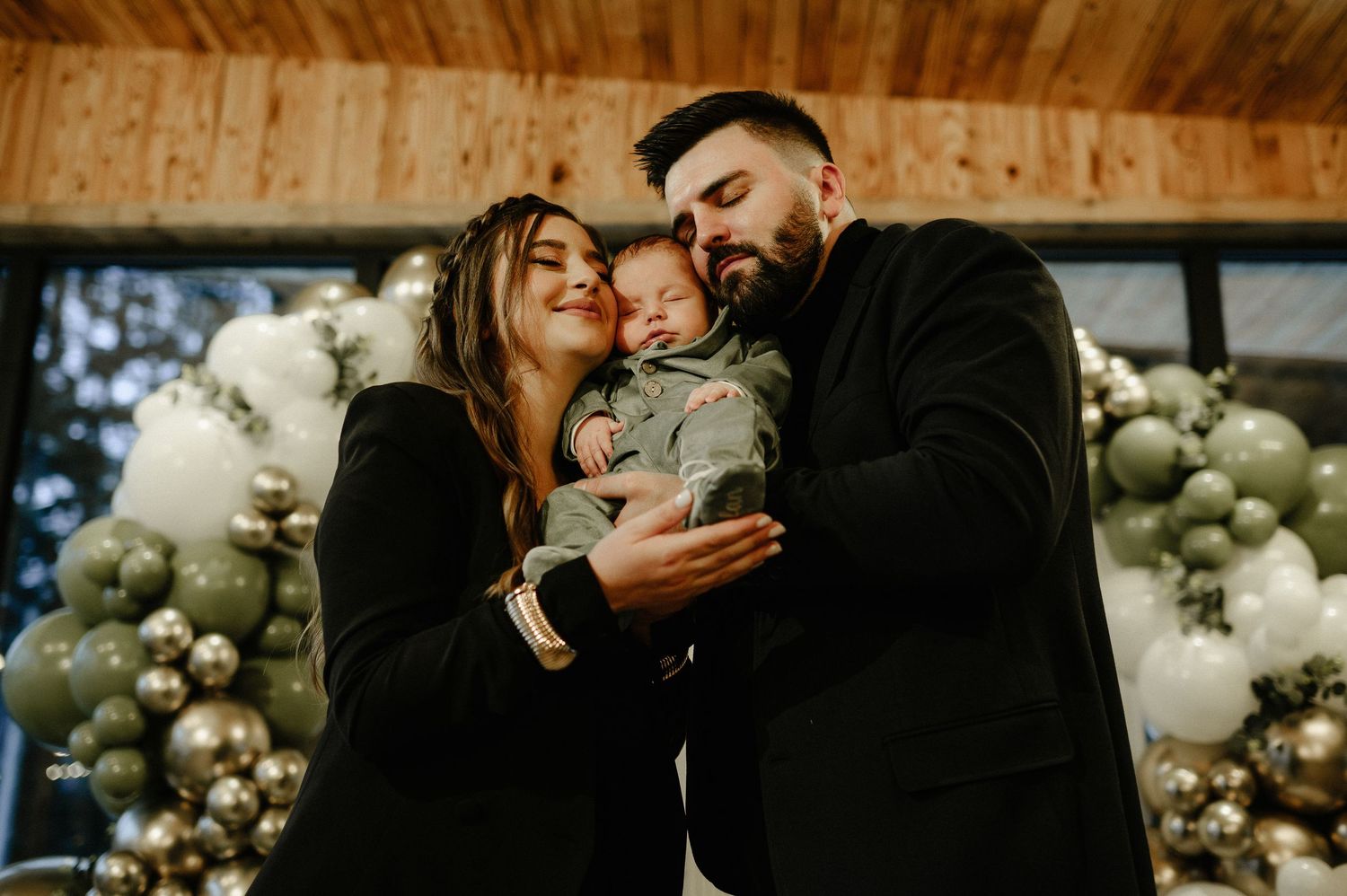 Proud parents lovingly gazing at their newborn baby at an elegant woodland-themed christening party with balloon decor.