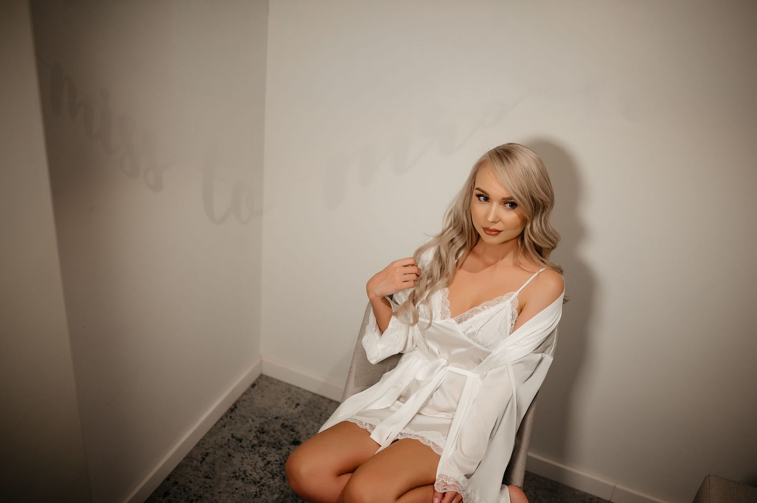 Blonde bride in a white silk robe sitting on the floor during bridal boudoir photography session.