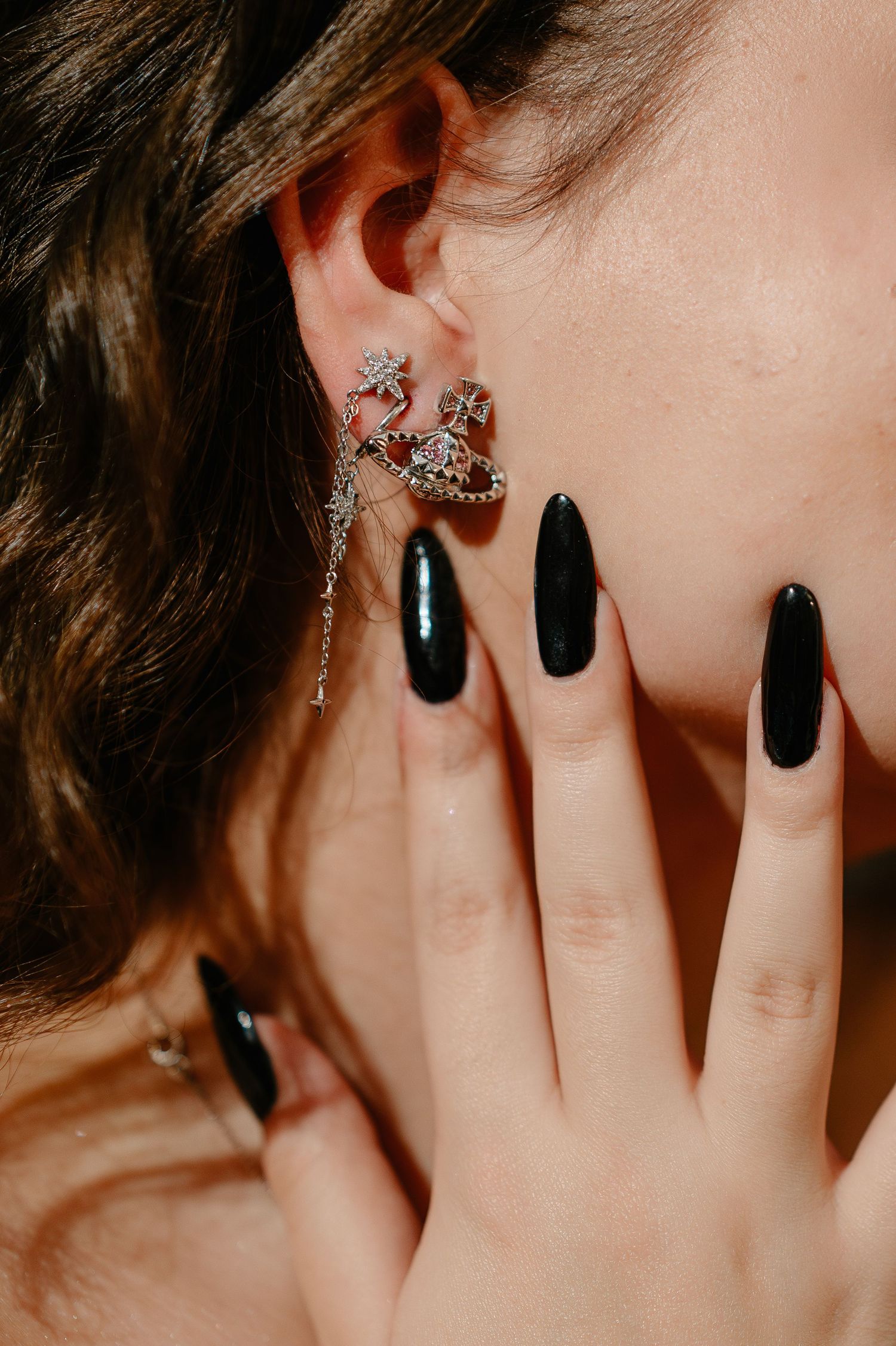 Close-up of decorative crystal earring and black stiletto nails against womans cheek.