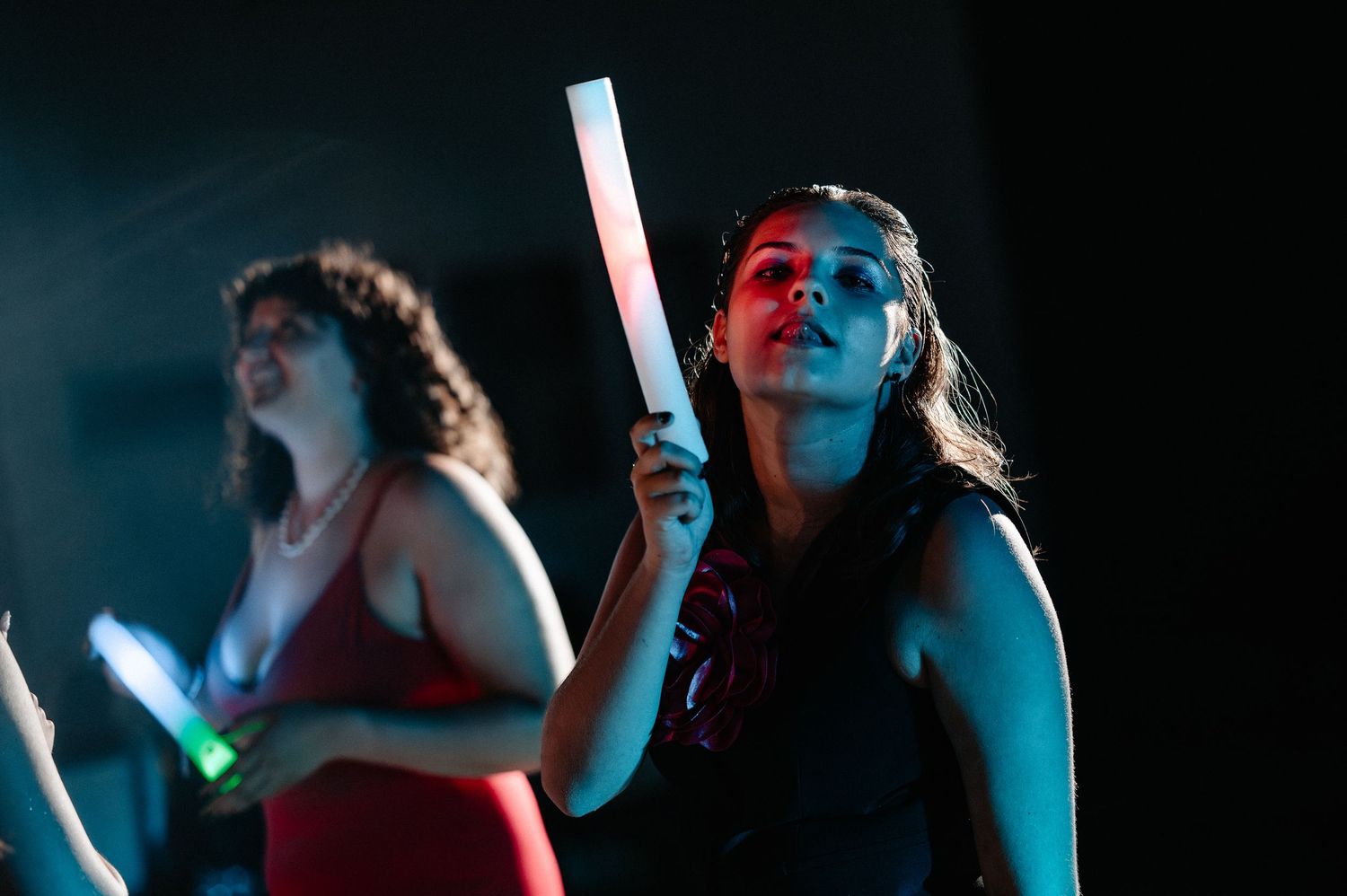 Two young women dancing with glow sticks at a vibrant nighttime indoor event.