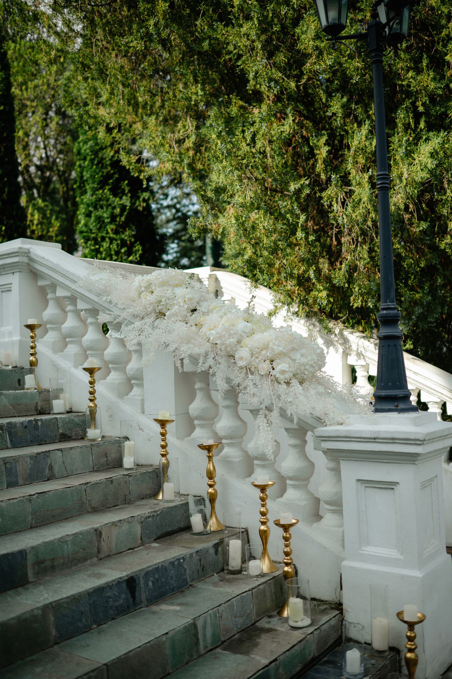 White staircase decorated with gold candleholders and white floral arrangements for a wedding.
