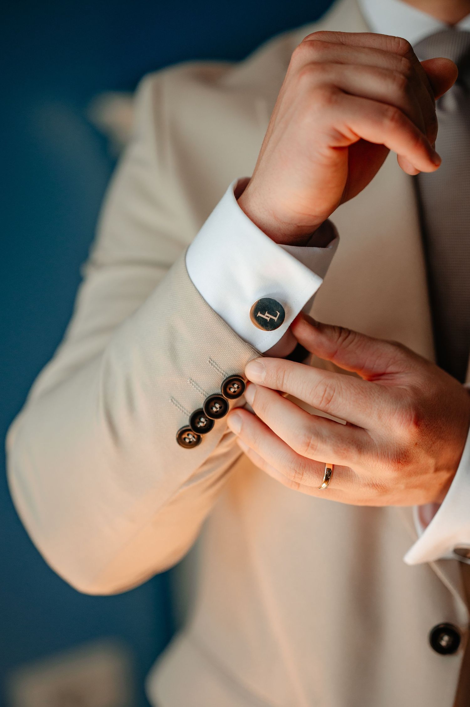 Groom adjusting cufflinks on white shirt sleeve in beige wedding suit.