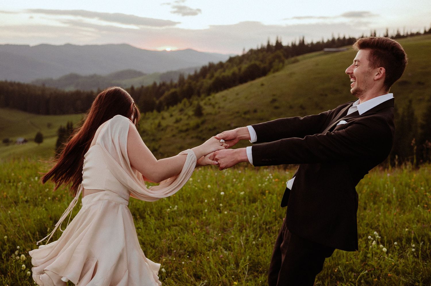 Couple spinning and laughing together in a wildflower meadow with mountain views at golden hour.
