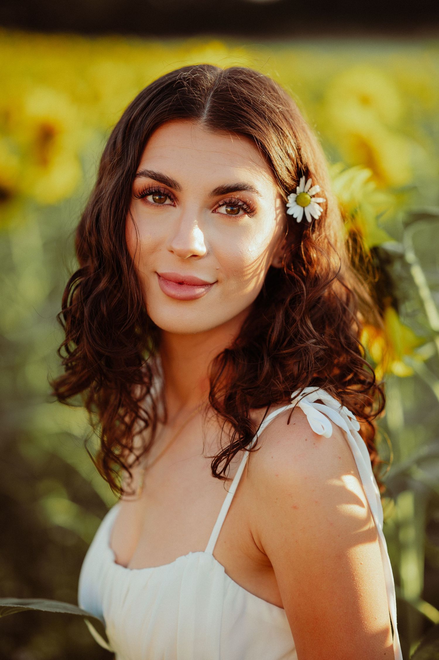Beautiful brunette woman with daisy hair accessory smiling in a sunlit sunflower field.