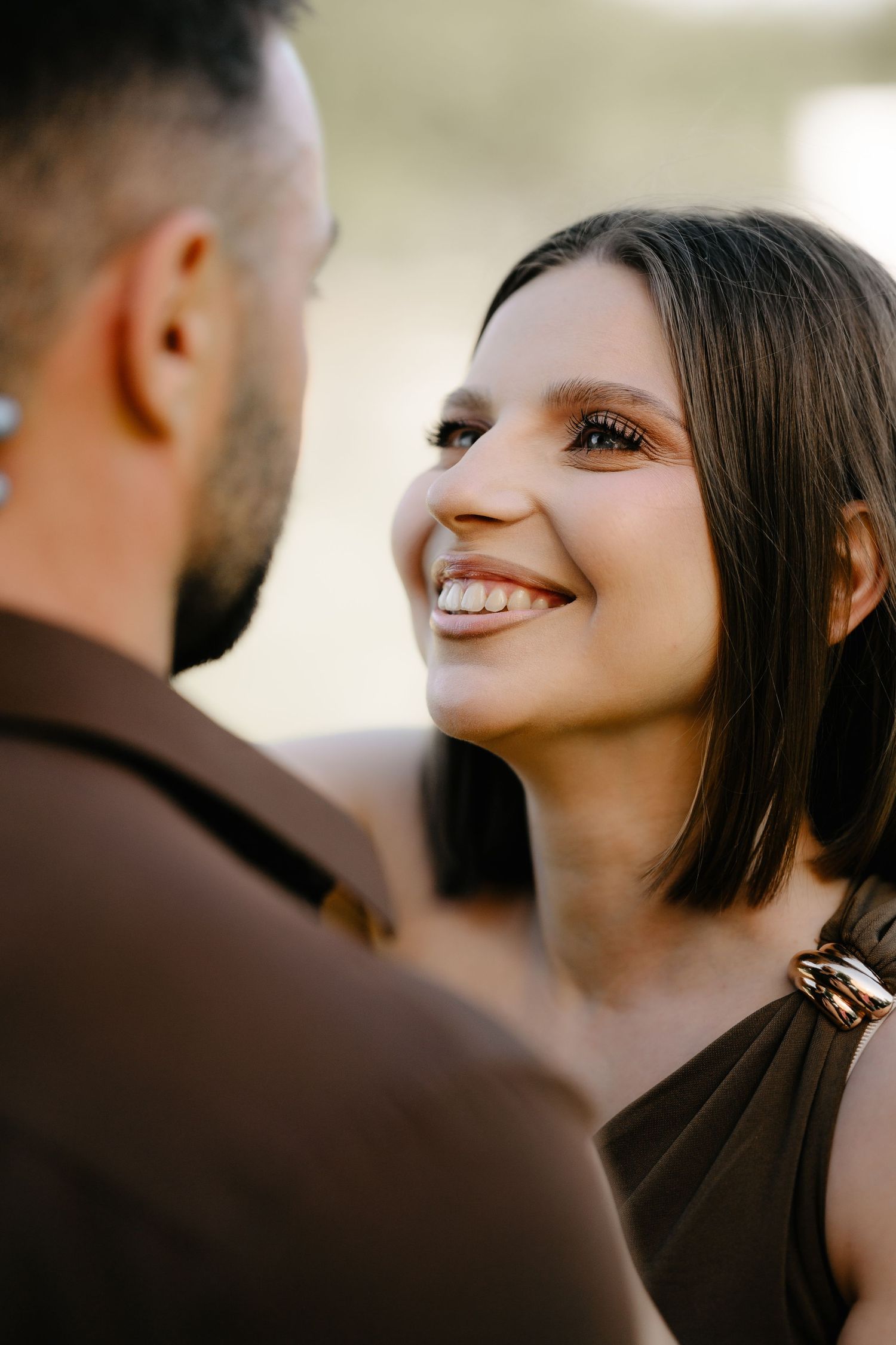 Smiling brunette woman with short hair gazes at a bearded man in a romantic outdoor portrait.