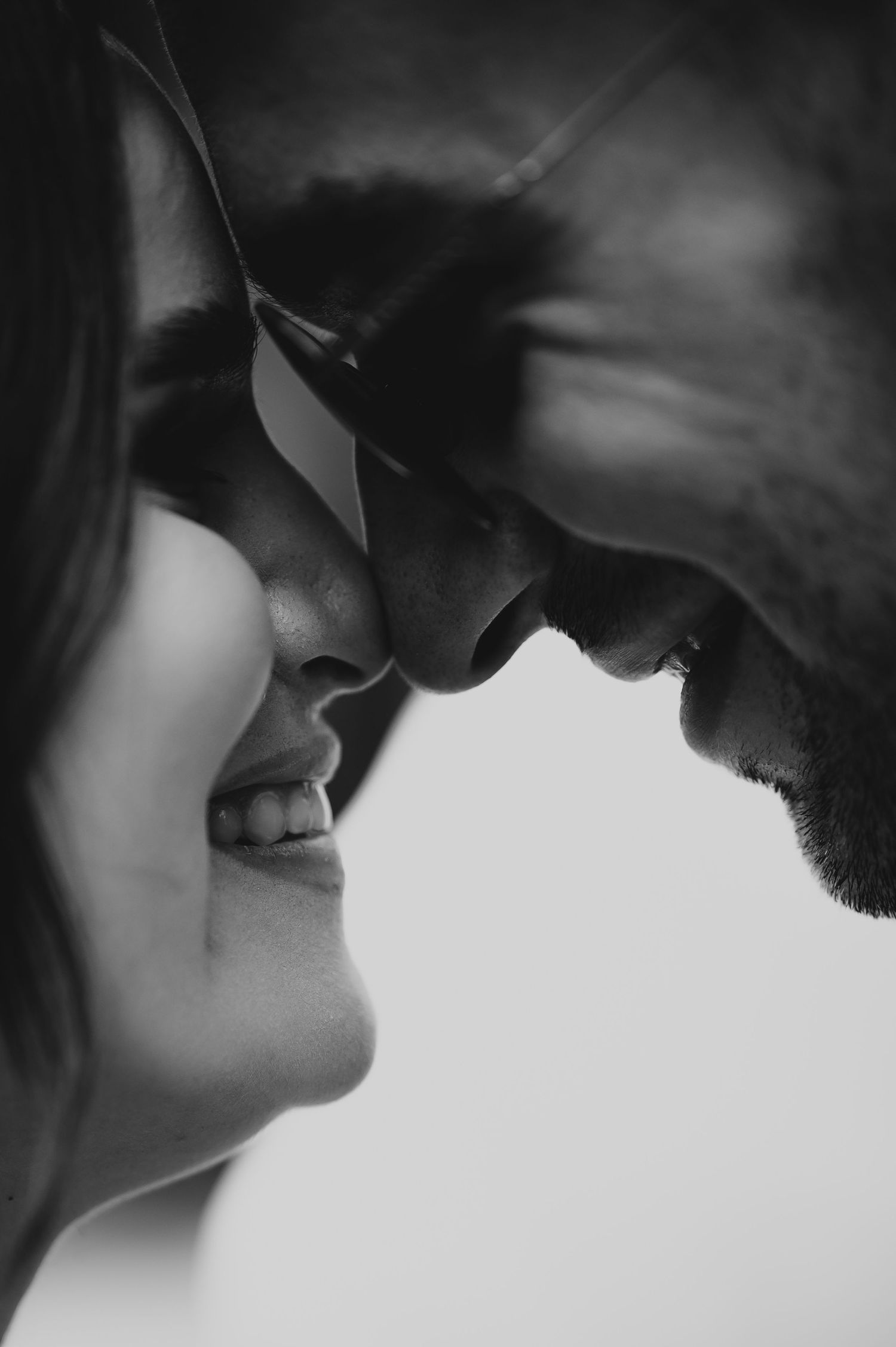 Romantic black and white close-up of couple nearly kissing, man wearing sunglasses.