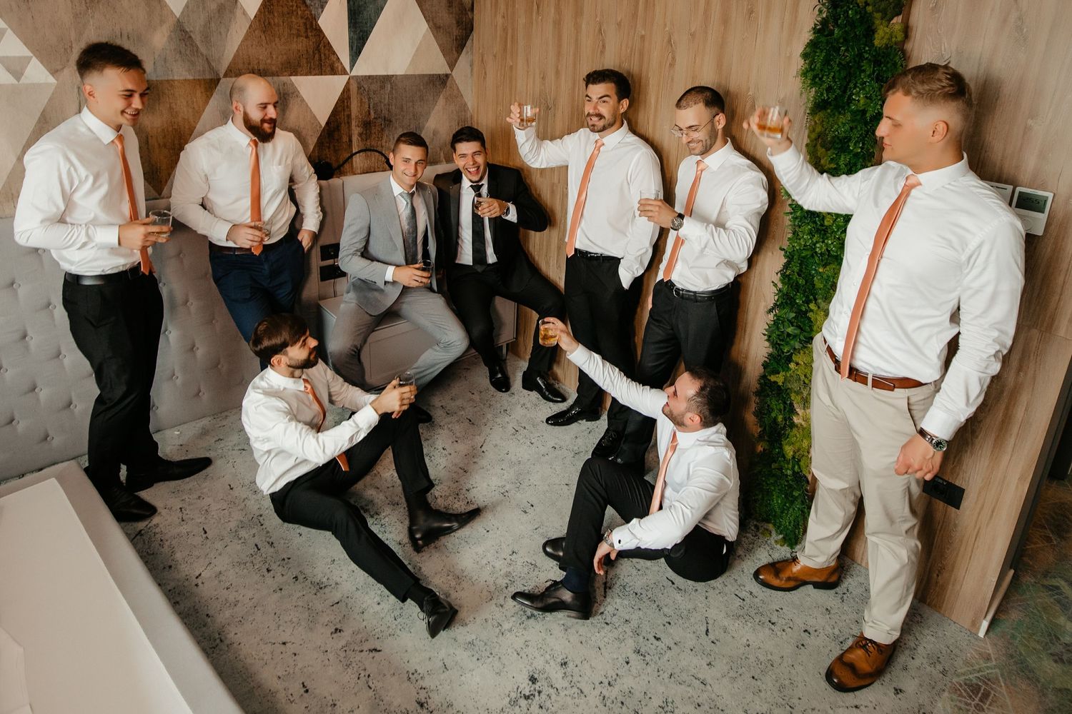 Large group of groomsmen in white shirts and dark pants pose playfully together before wedding ceremony.