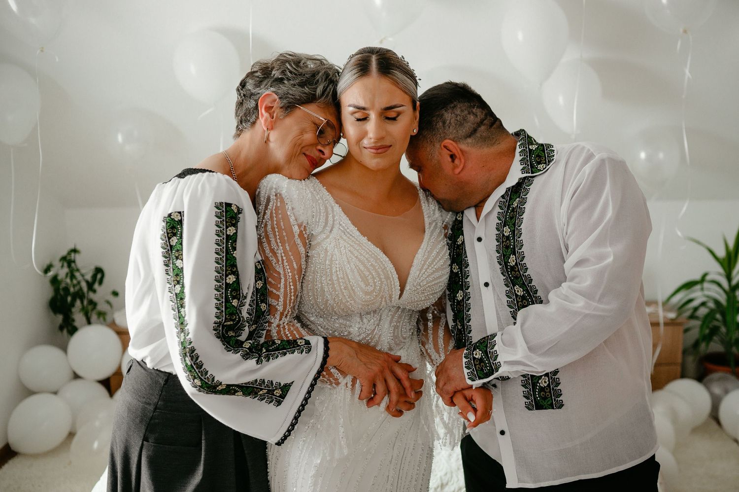 Parents in traditional Romanian embroidered shirts tenderly holding hands with bride in beaded wedding gown.