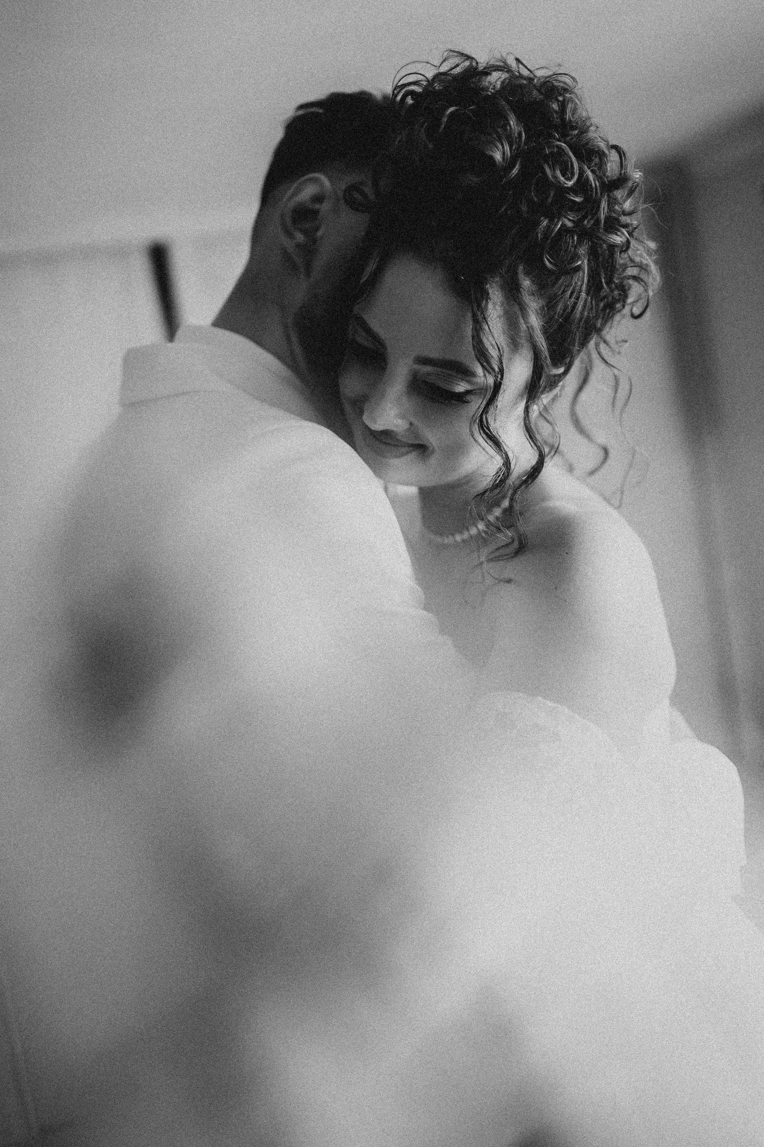 Black and white wedding photo of bride and groom embracing tenderly, bride smiling in elegant gown.