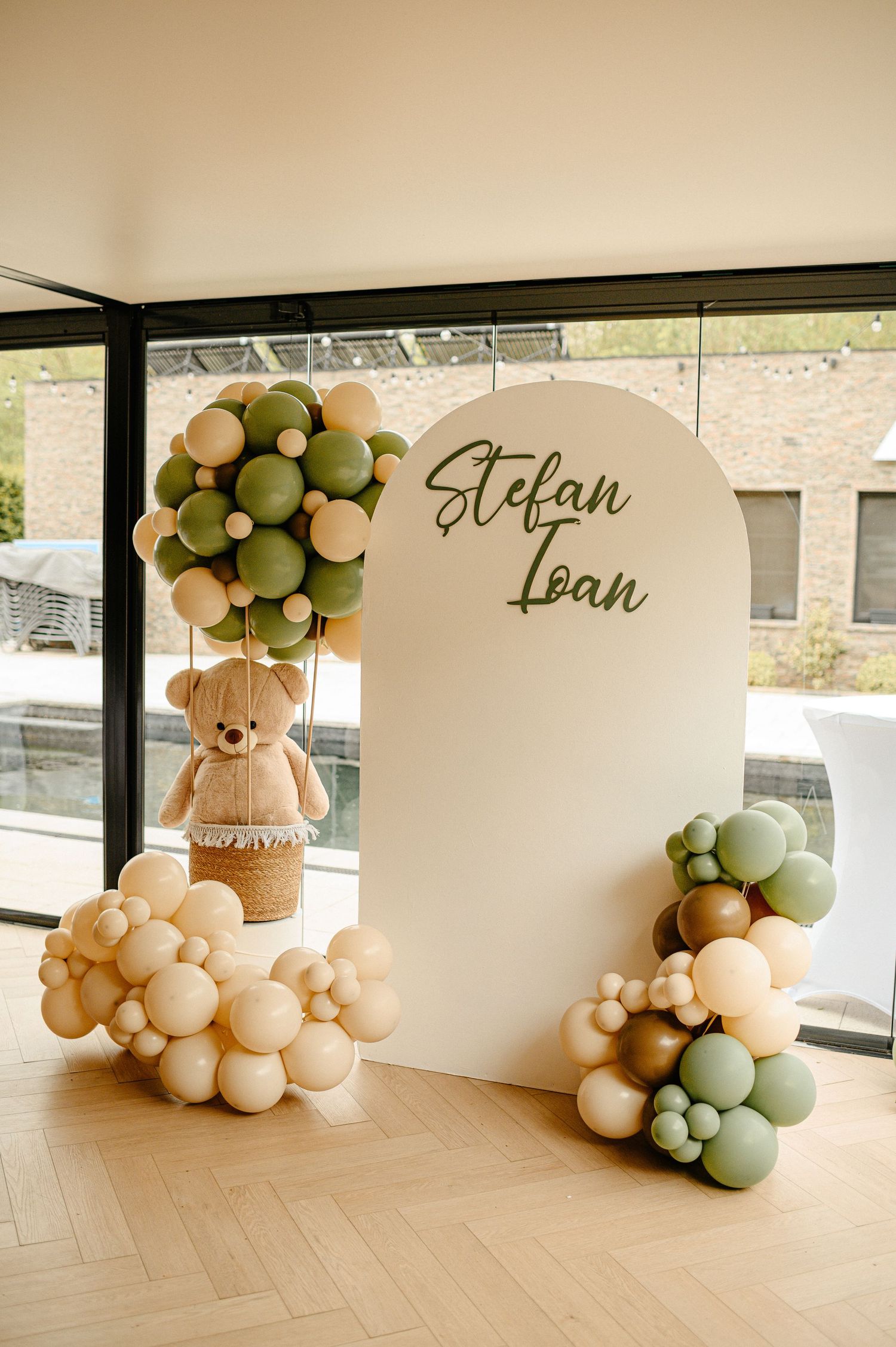 Baptism party backdrop with teddy bear balloon display and Stefan Ioan name sign.