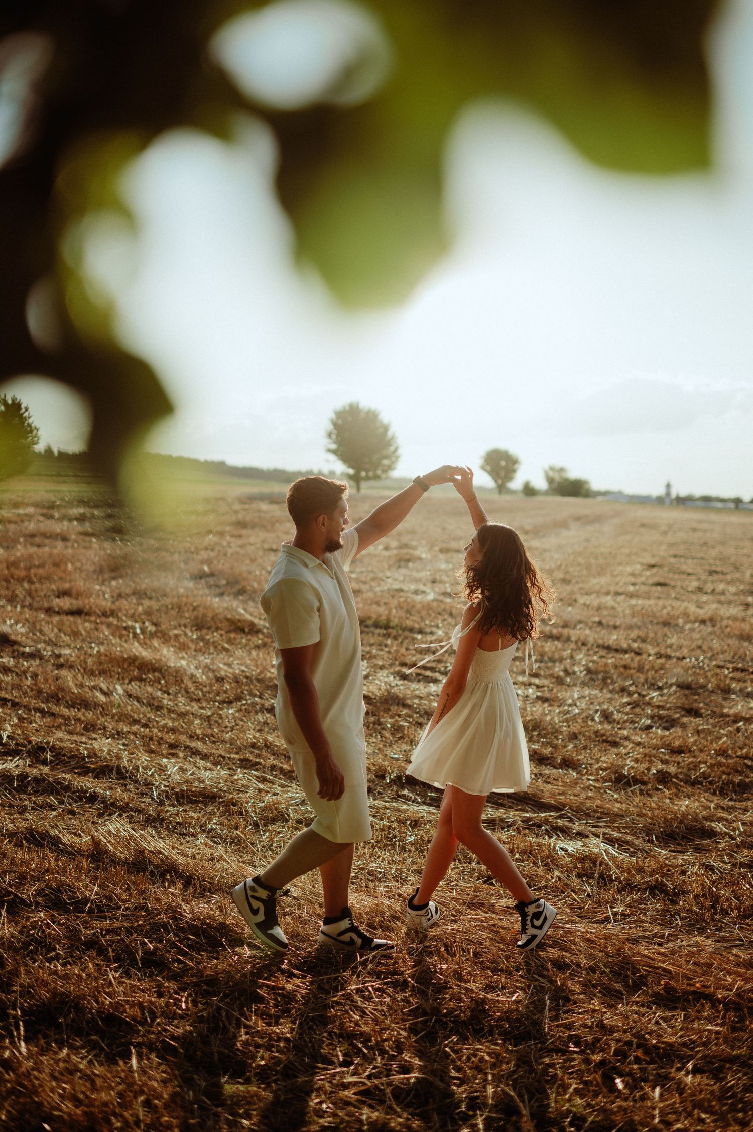 Couple dancing together in a sunlit harvested field at sunset.