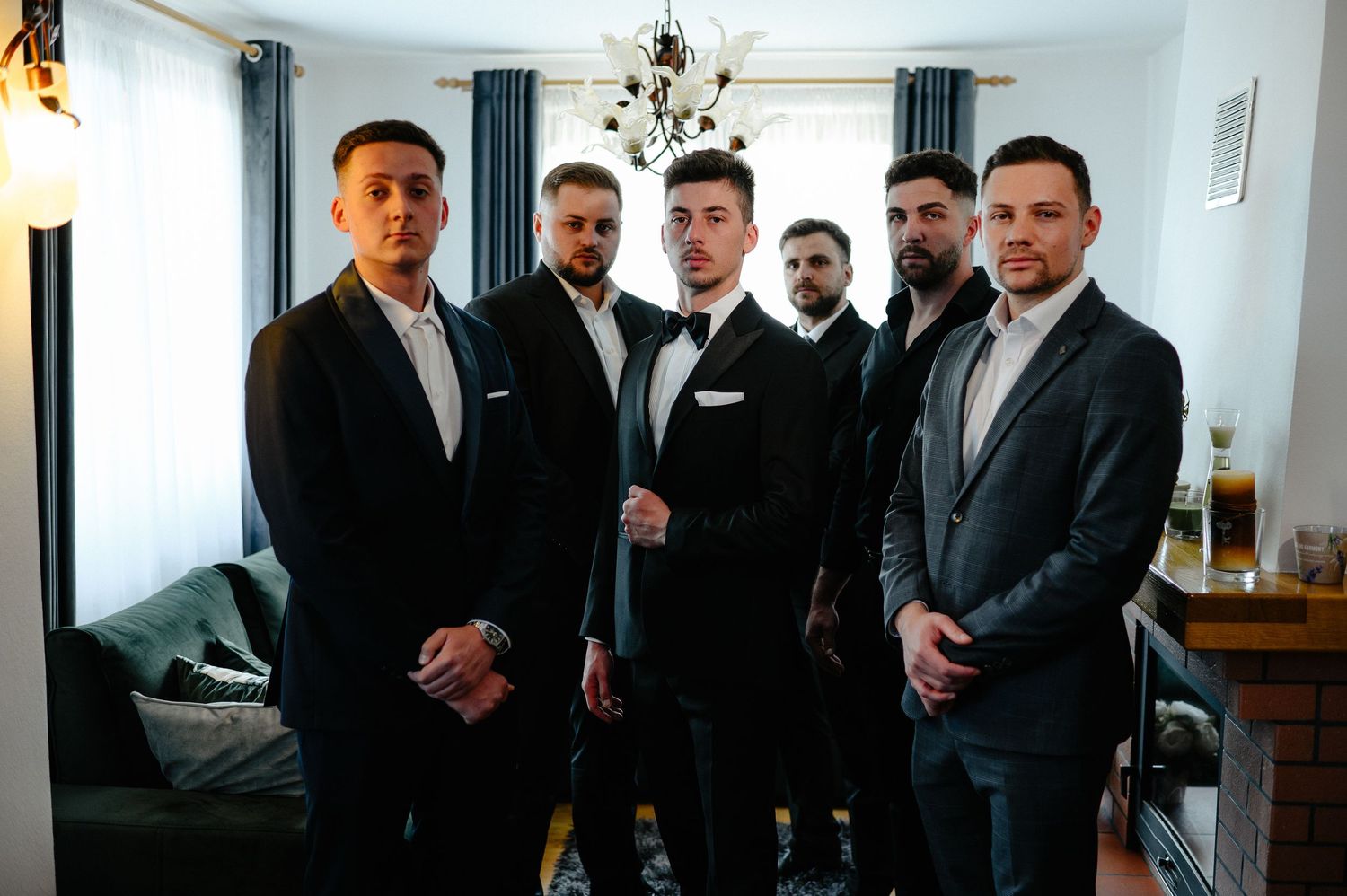 Group of five groomsmen in dark suits posing together indoors before wedding ceremony.