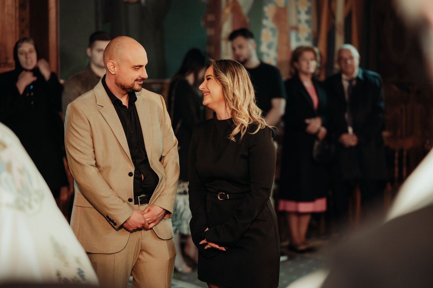 Couple standing together in a decorated Orthodox church during a baptism ceremony.