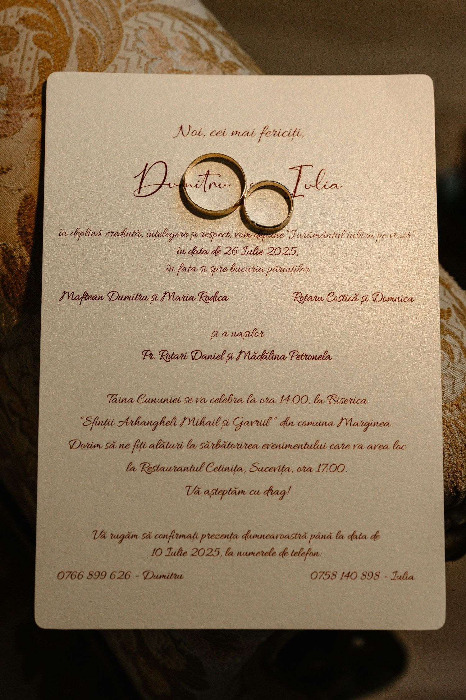 Gold wedding rings rest on an elegant Romanian wedding invitation for Dumitru and Julia, dated July 26, 2025.