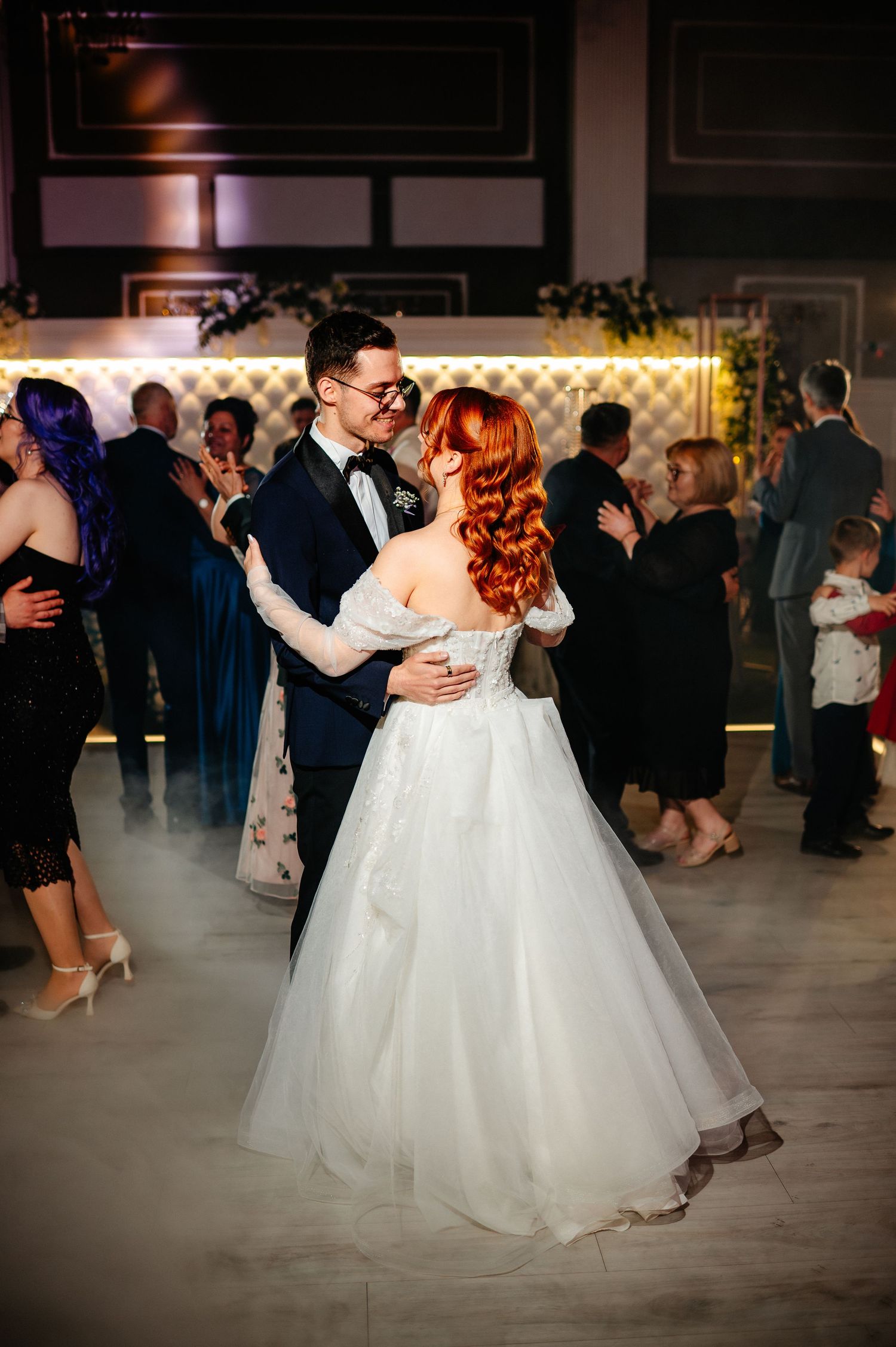 A bride and groom share their first dance, surrounded by guests in an elegant wedding reception venue.