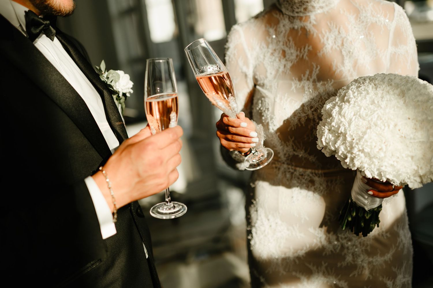 Bride and groom toasting with champagne flutes, bride holding white bouquet in lace wedding dress.