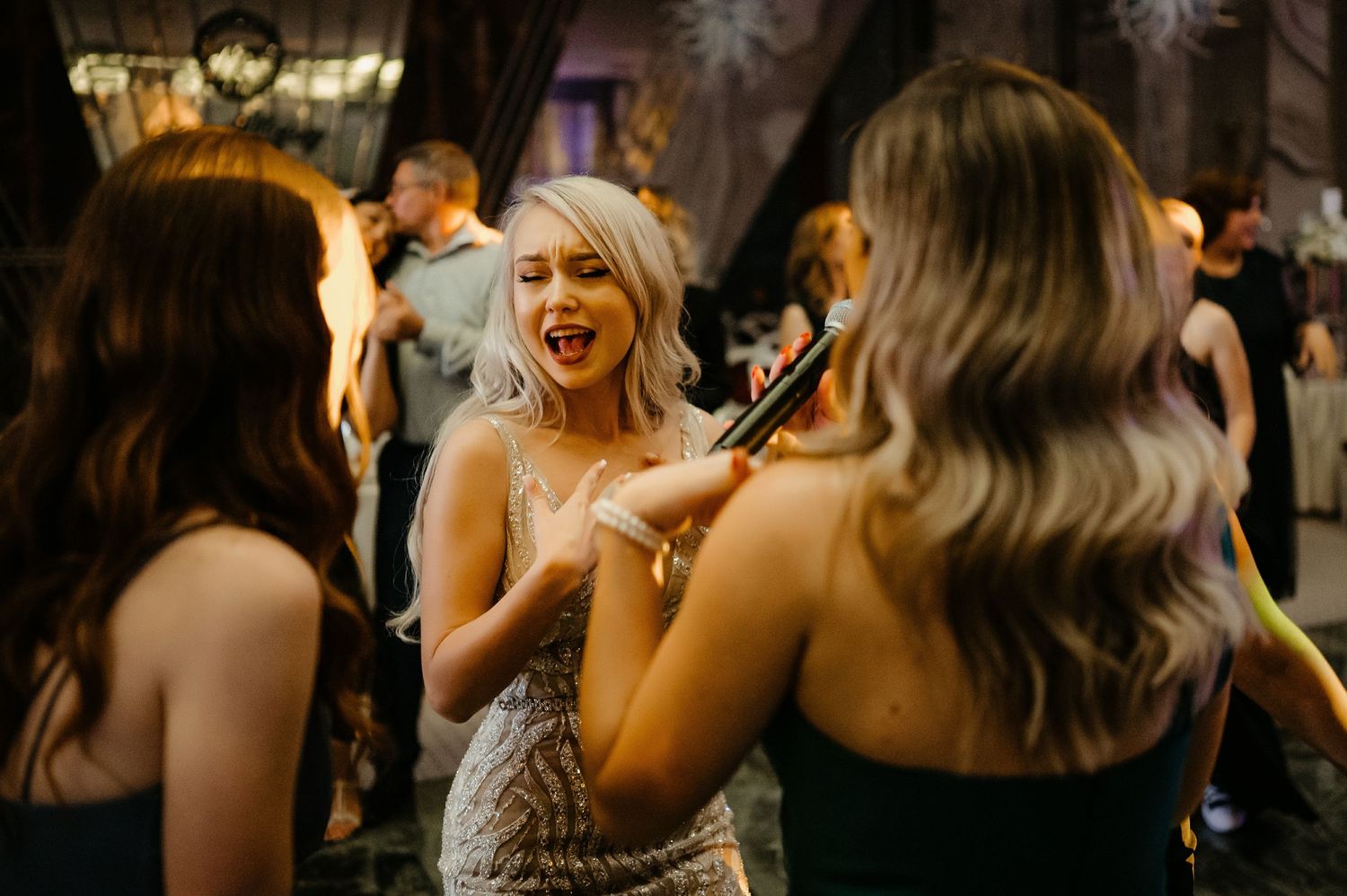 Bride in sequined dress laughs joyfully with friends on the wedding reception dance floor.
