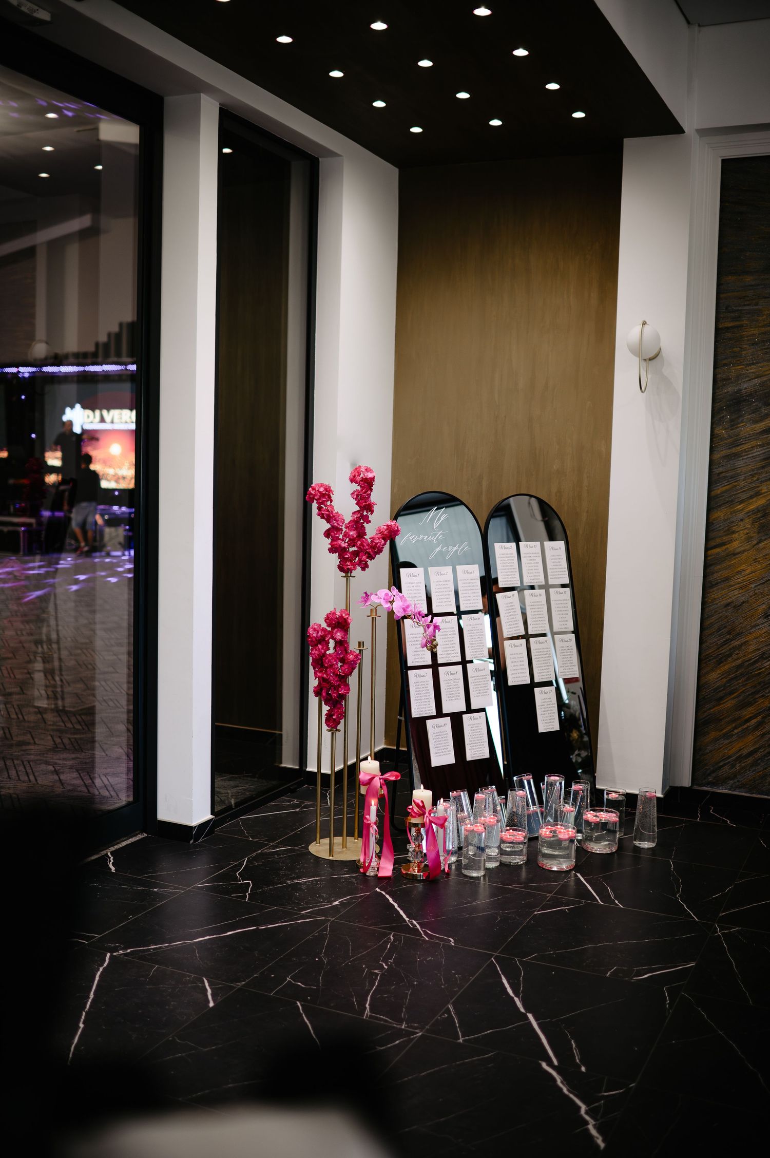 Wedding lobby display with arched mirrors seating chart and pink floral arrangements.