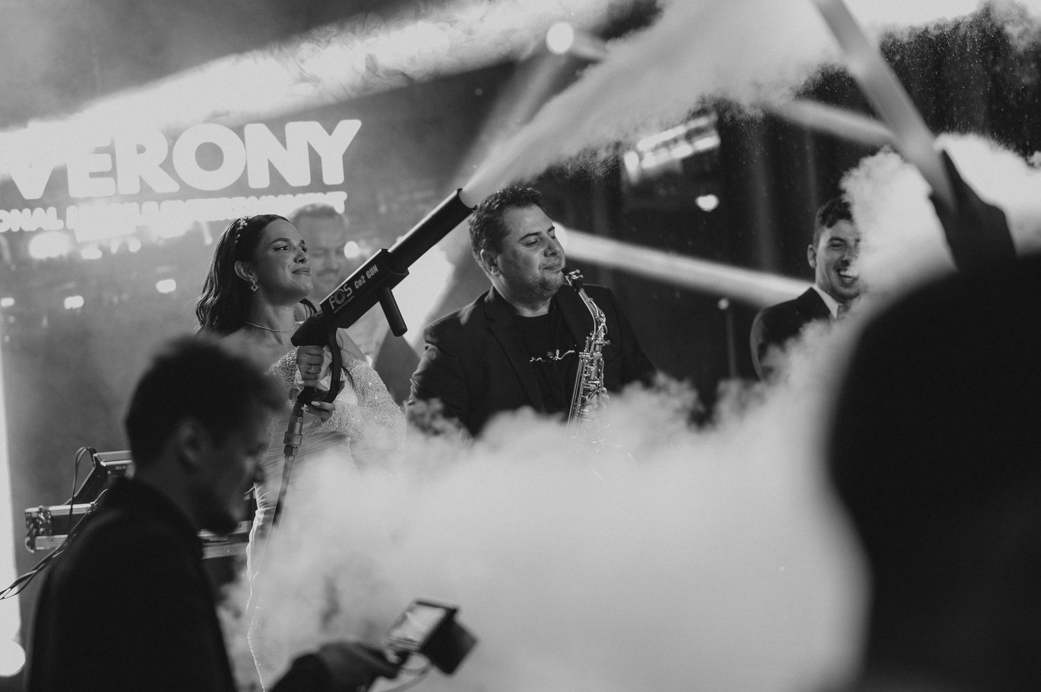 Black and white photo of DJ Verony performing live with smoke effects at an energetic music event.