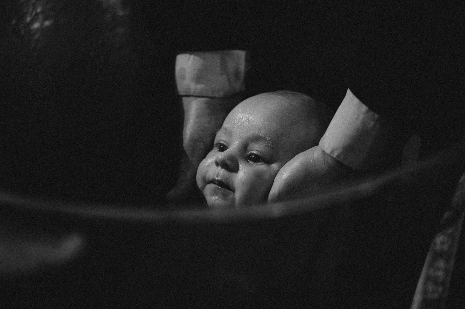 A peaceful newborn baby rests in caring hands in a tender black and white photograph.