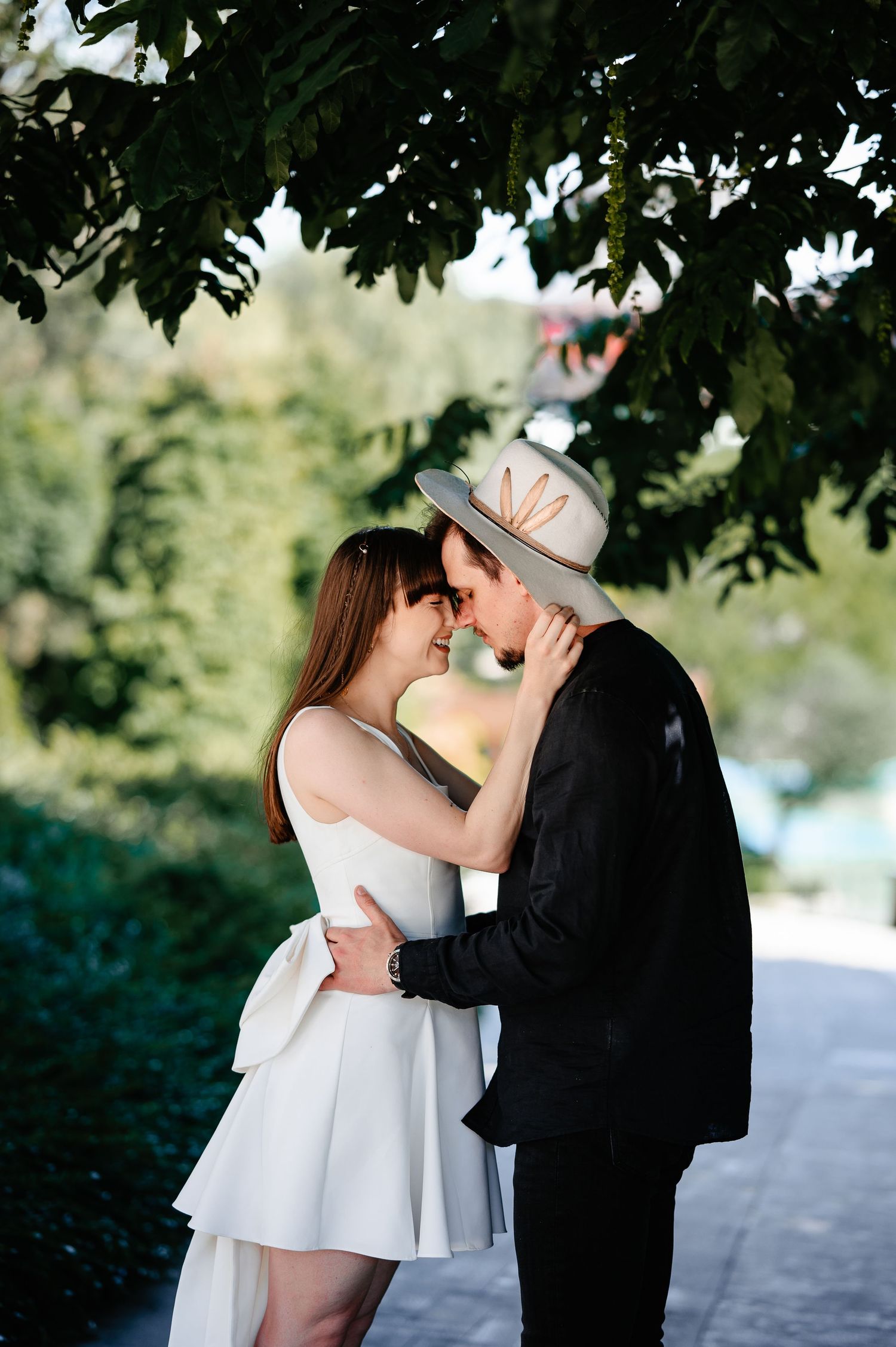Loving couple sharing a tender moment about to kiss under lush green tree branches.