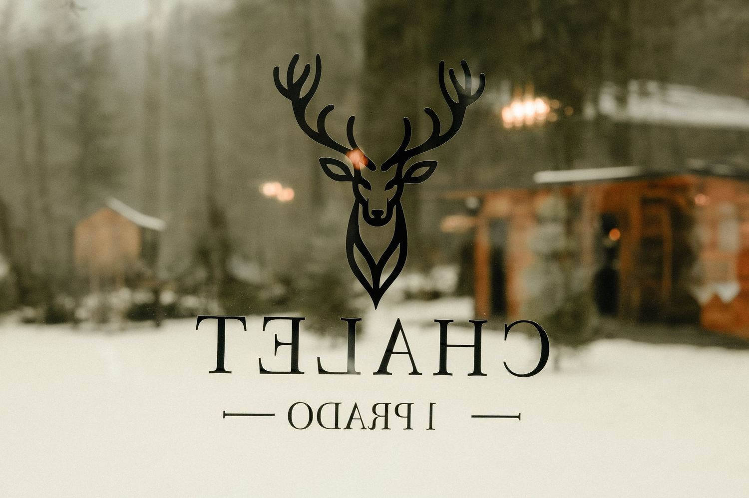 Chalet Prado logo with deer antler design on snowy winter window reflection.