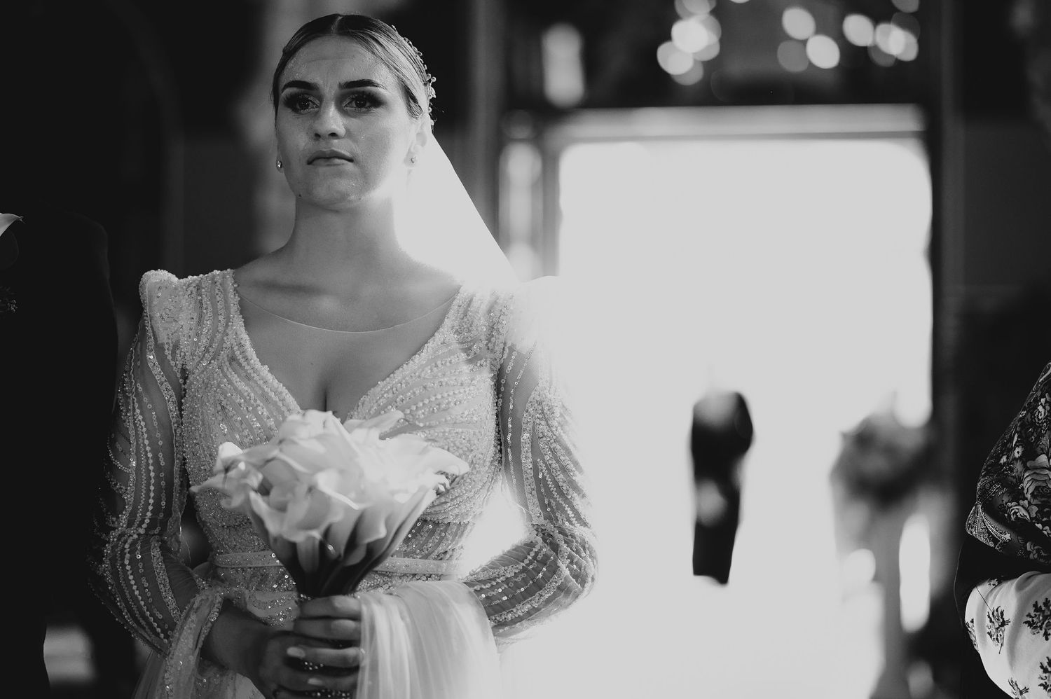 Black and white portrait of a beautiful bride wearing a beaded wedding dress and veil holding a white bouquet.