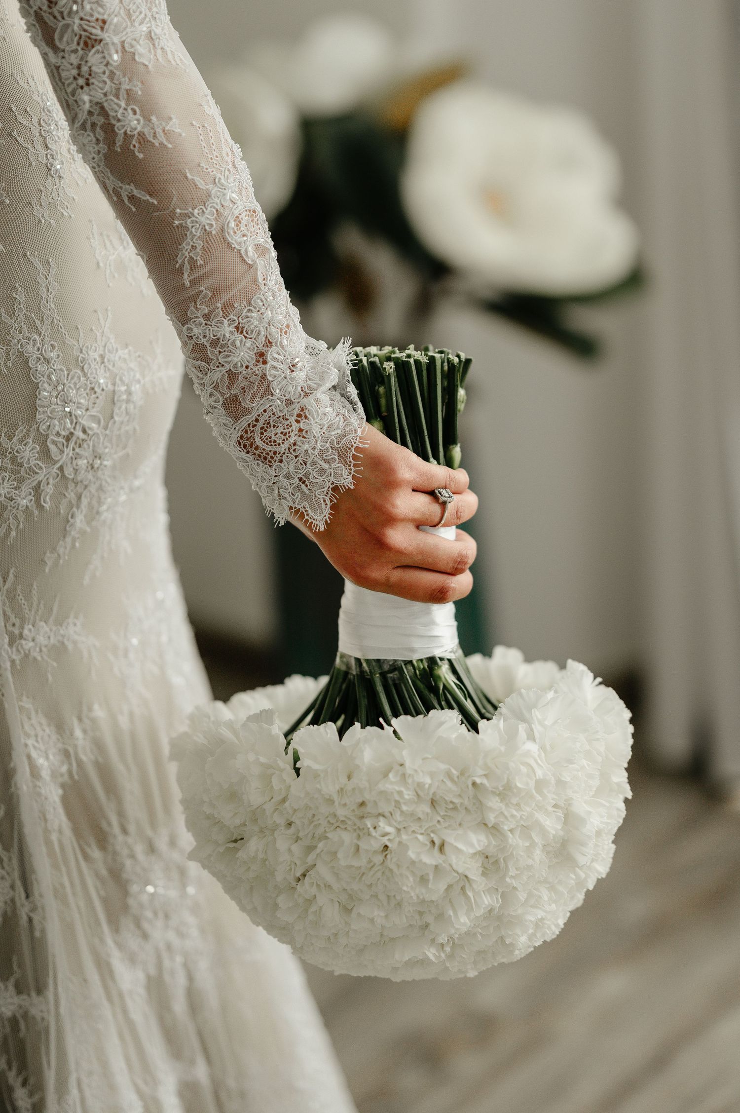 Close-up of bride holding elegant round white hydrangea bouquet in lace wedding dress.
