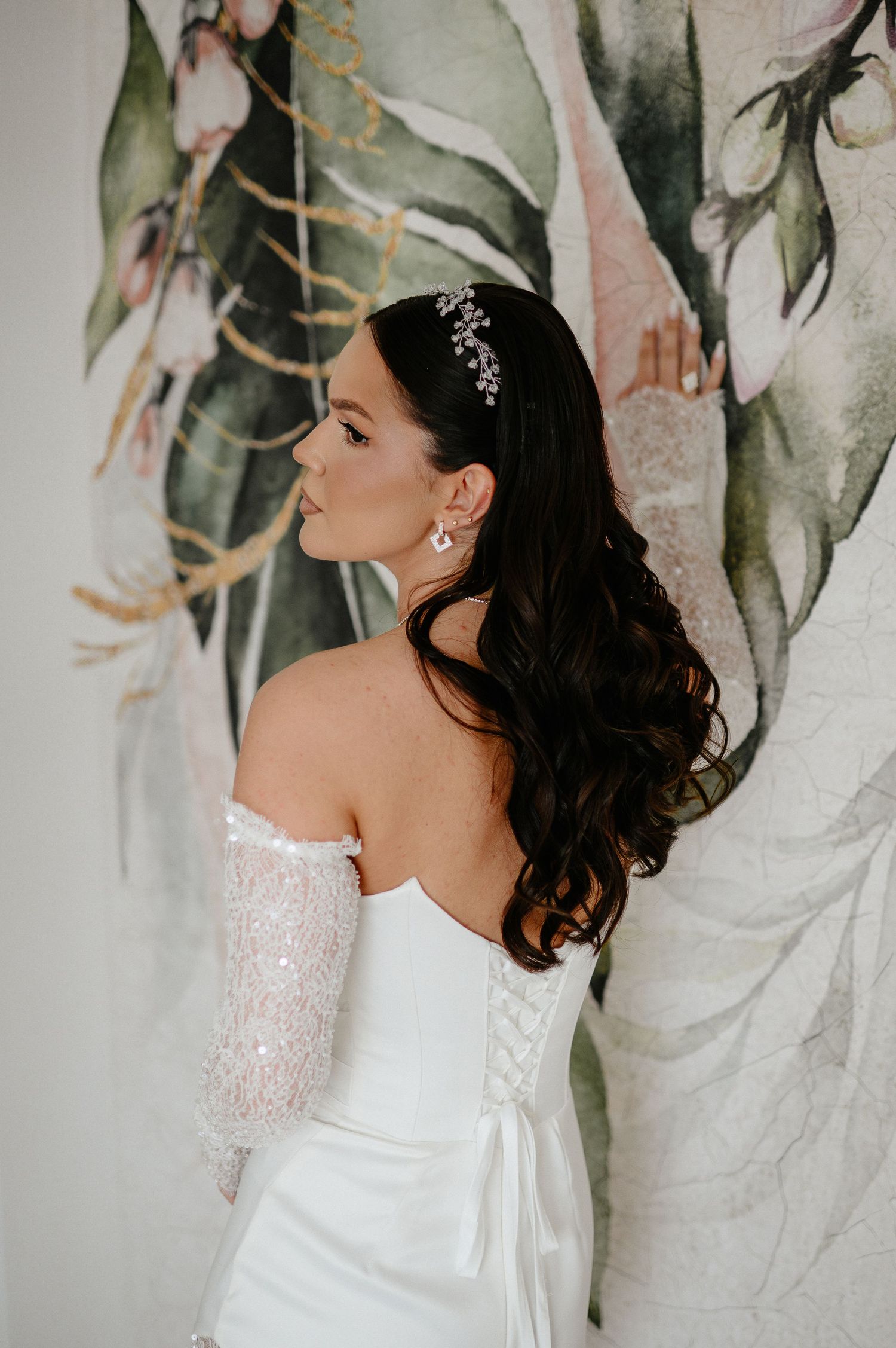 Bride in strapless white gown with beaded sleeves shows elegant back hairstyle and earrings.