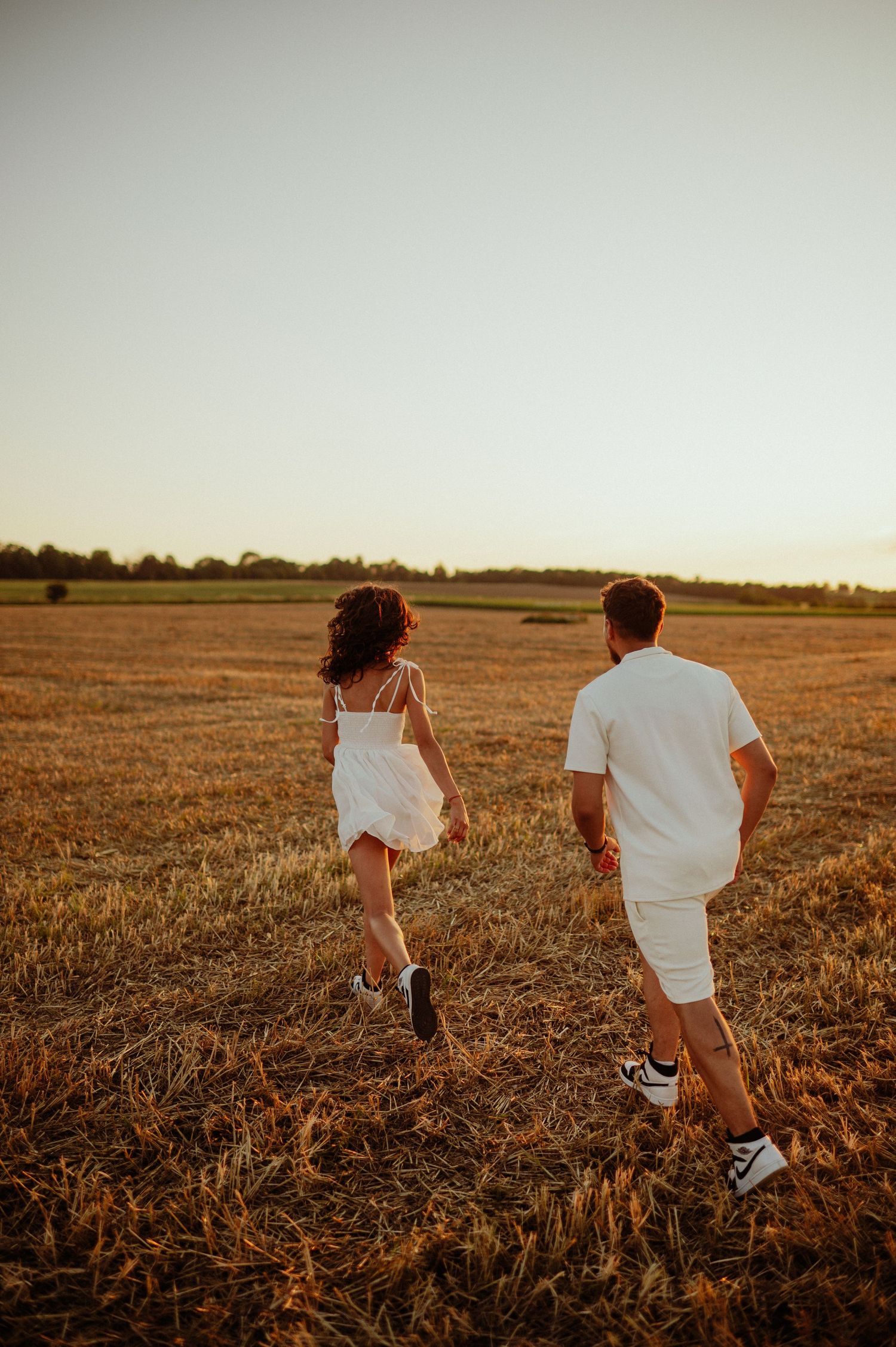 Couple running hand in hand through a golden harvested field during a warm sunset.