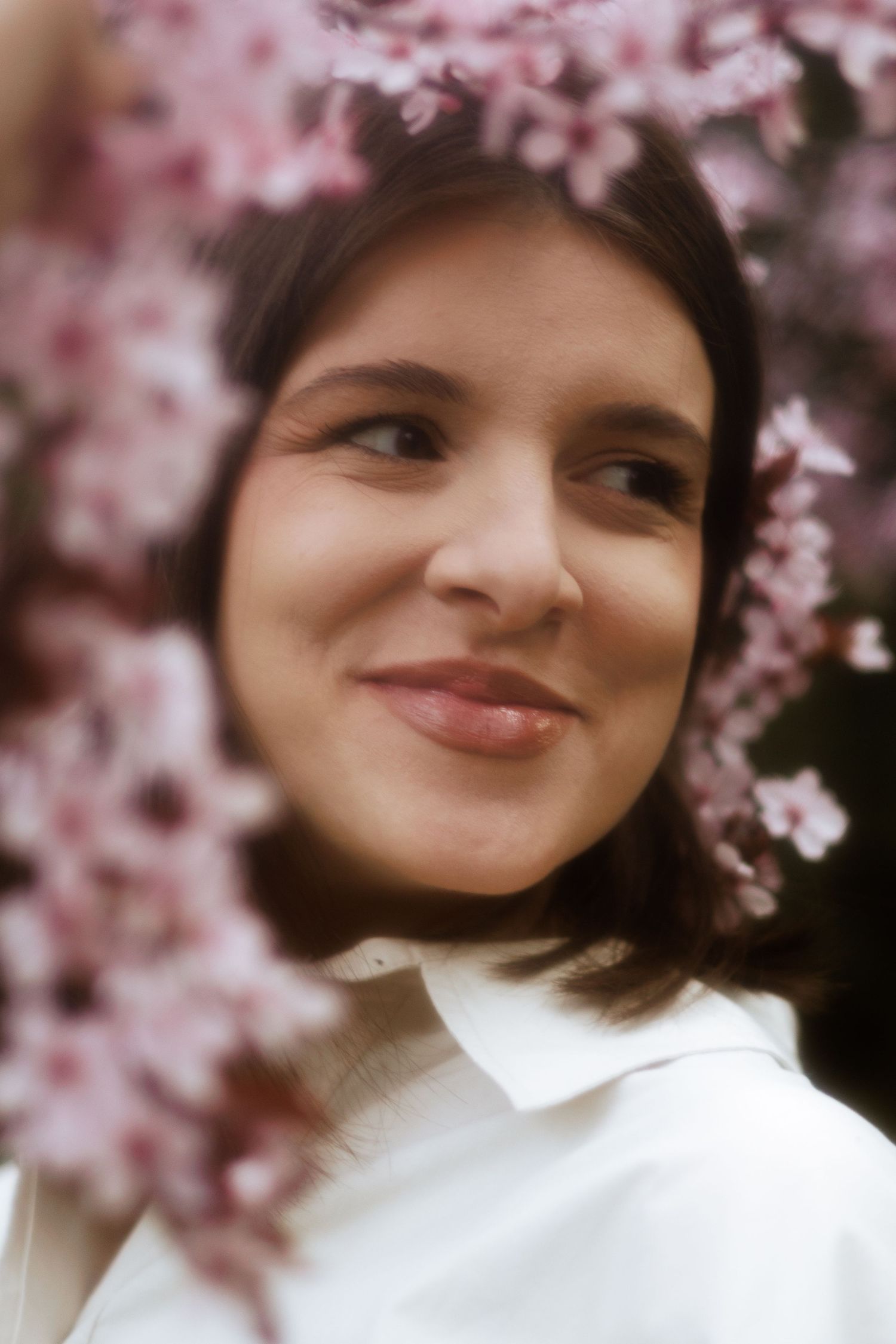 Close up portrait of smiling young woman surrounded by pink spring cherry blossoms.